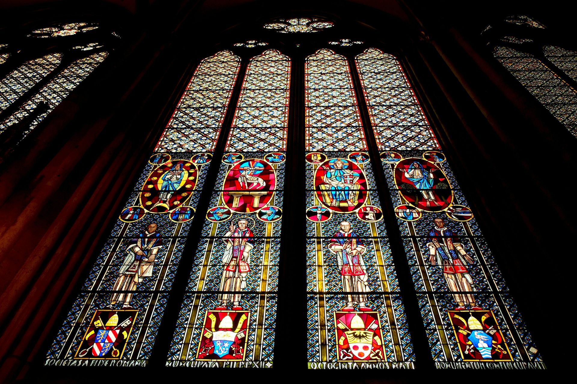 Stained glass window inside a dark building. Colorful figures and patterns in a gothic style, natural light.
