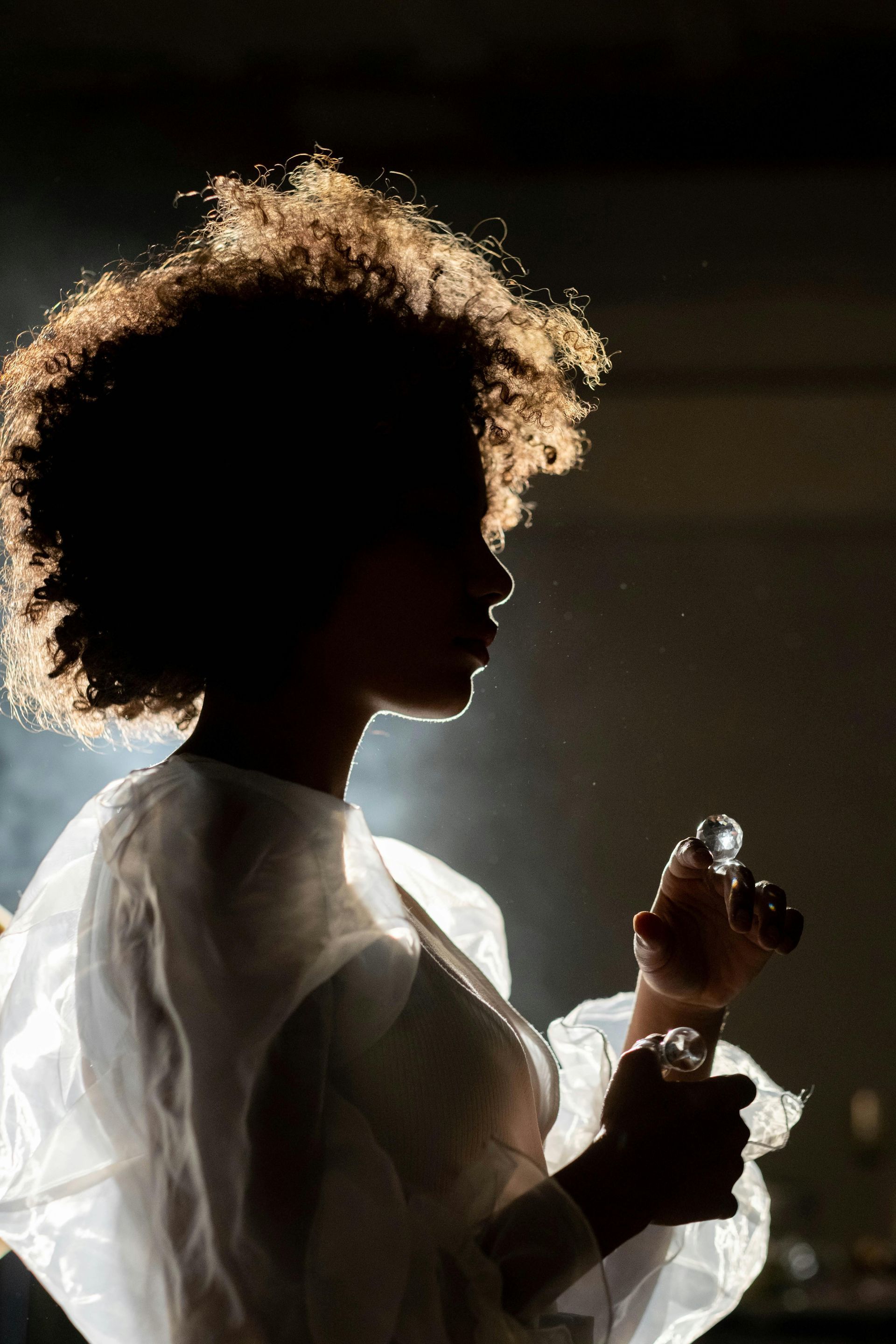Woman spraying mist, silhouette with bright hair, holding a small bottle.