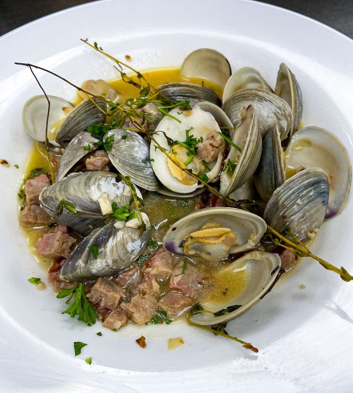 Clams cooked in broth, with sausage and herbs in a white bowl.