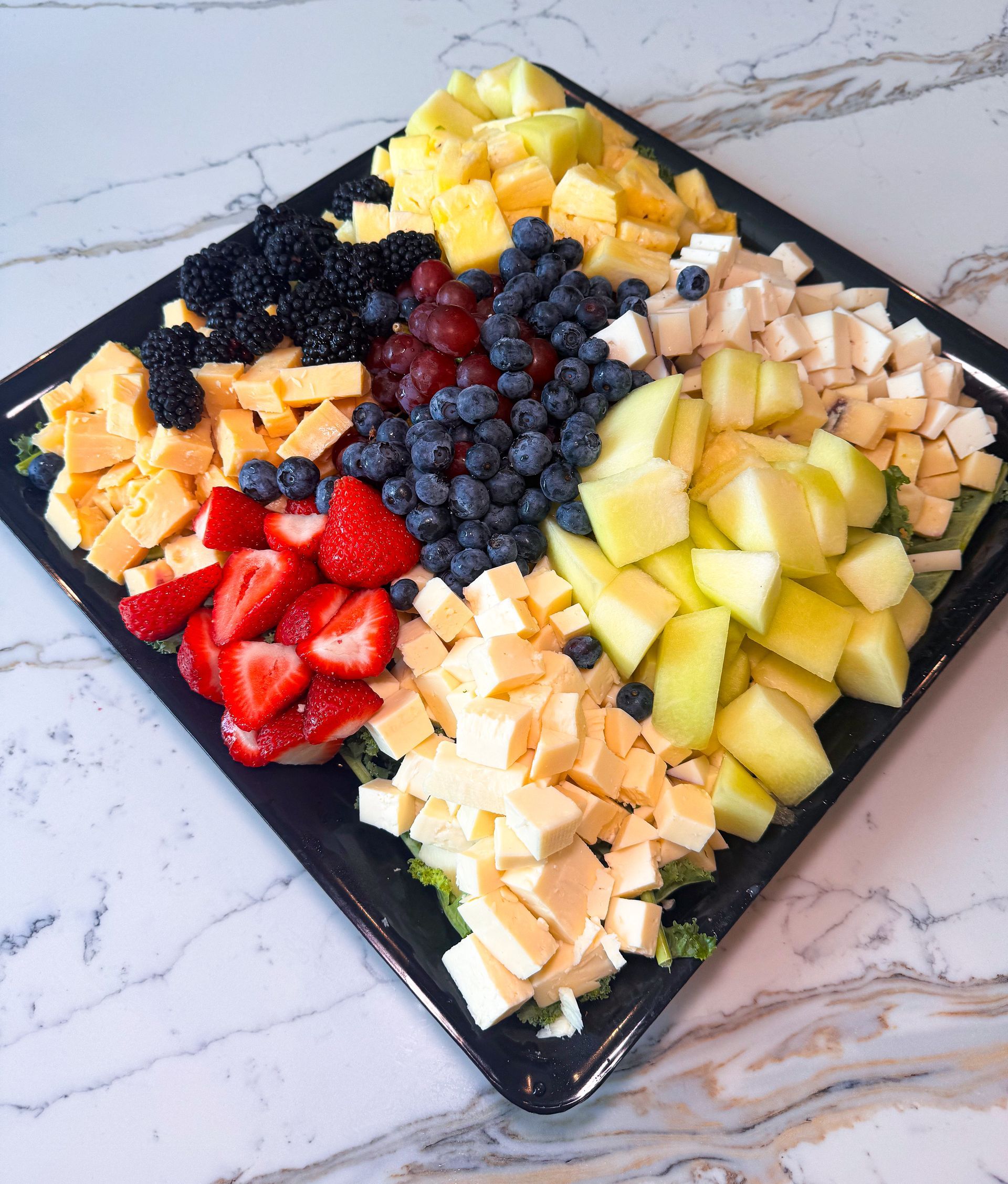 Square platter with a colorful arrangement of diced cheese, berries, and apples.