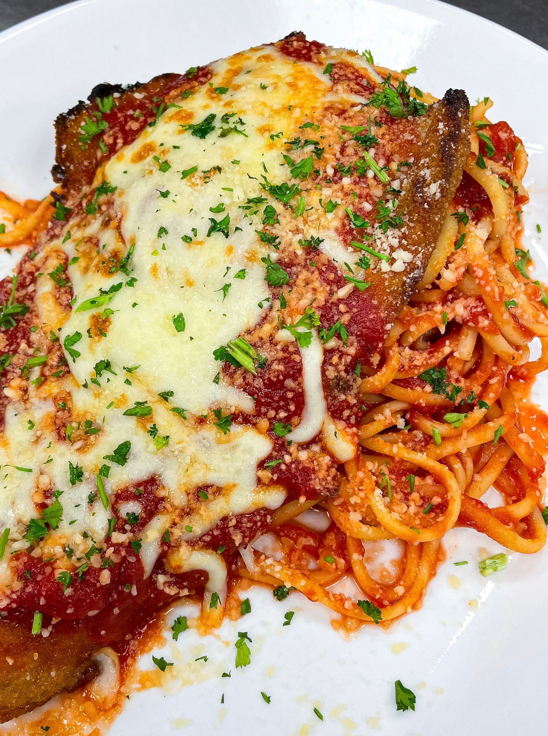 CHICKEN parmesan over spaghetti, topped with melted cheese and parsley garnish.
