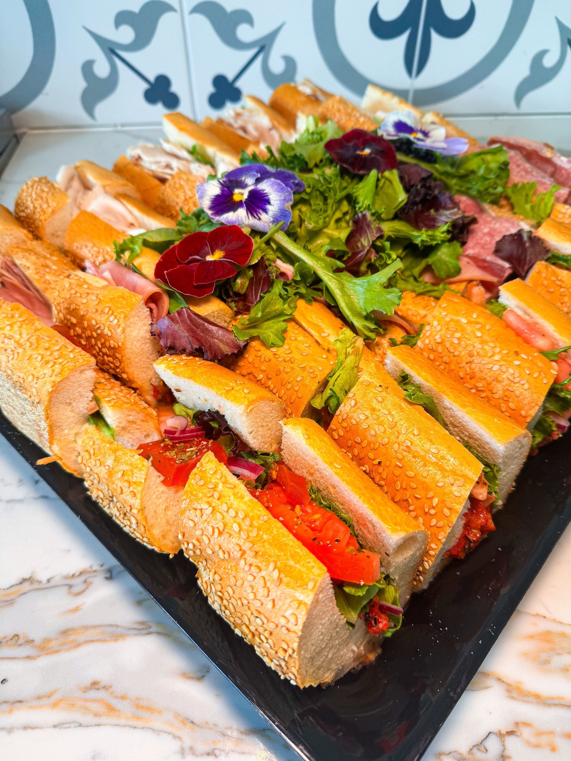 Assortment of sliced sandwiches on a platter with salad, decorated with edible flowers.