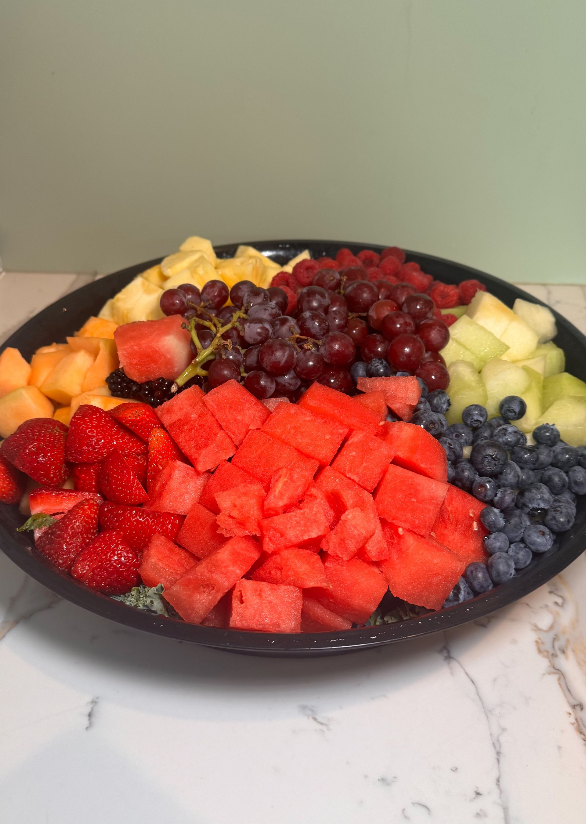 Fruit platter with assorted colorful fruit: strawberries, watermelon, grapes, melon, pineapple, blueberries.