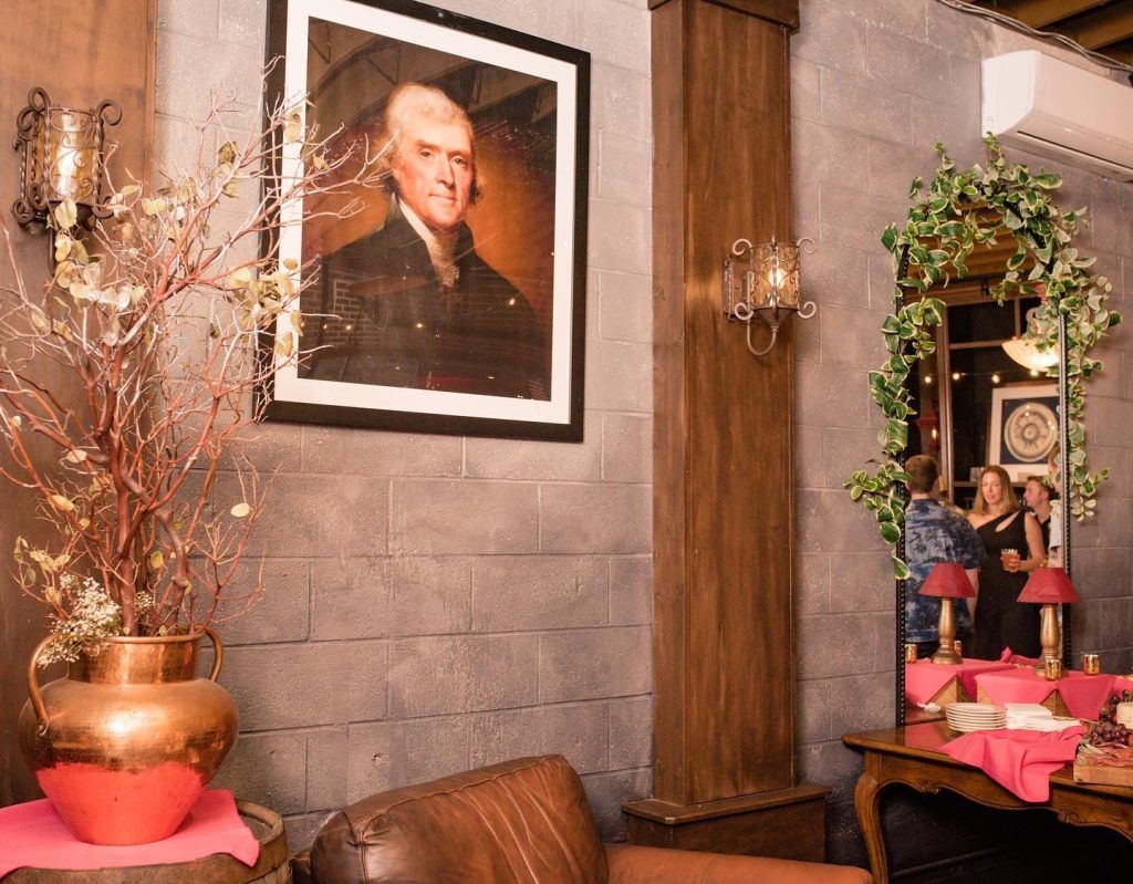 Interior with portrait, mirror, plants, and seating in a room with a decorative wall.