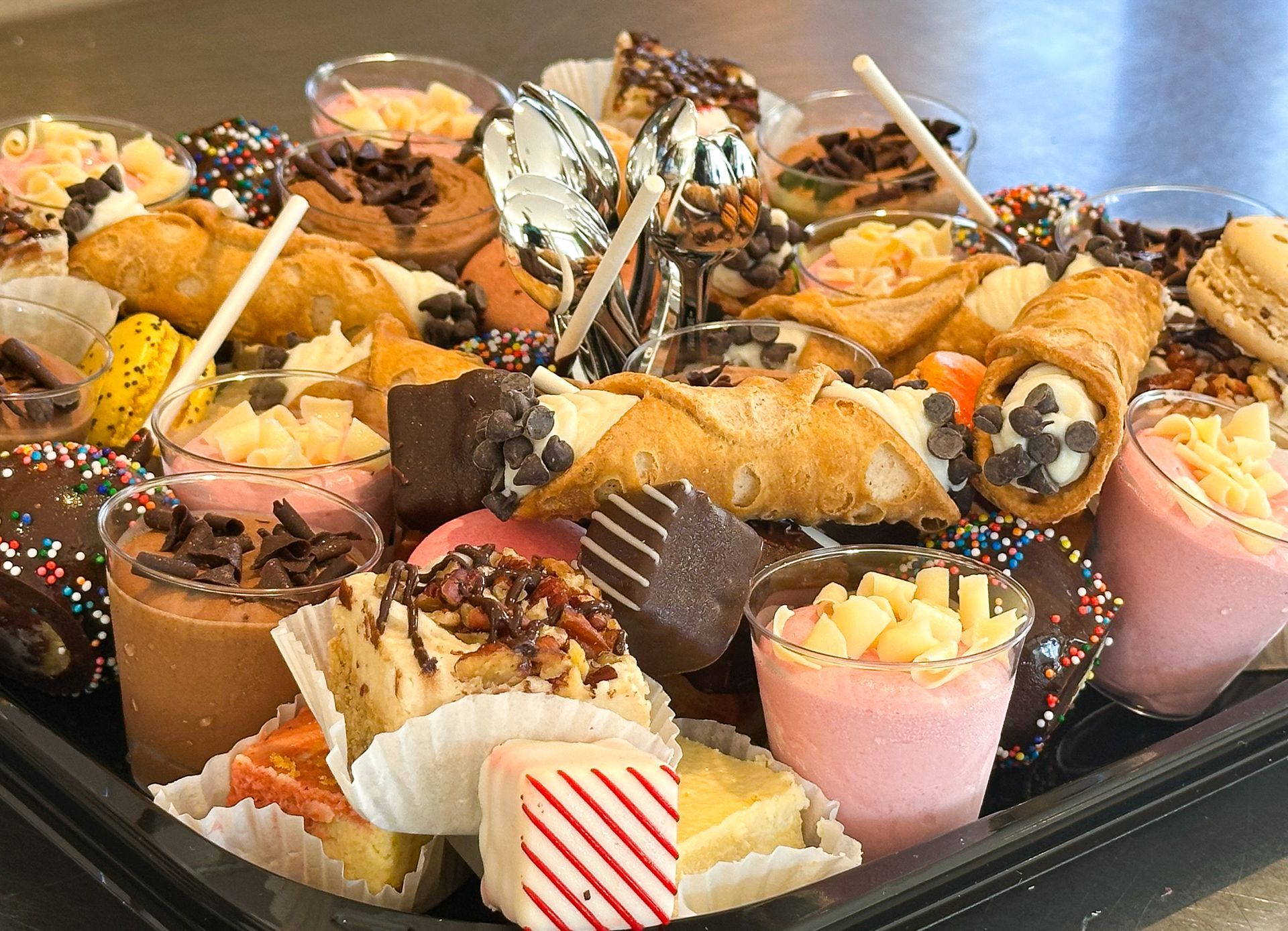 Tray of assorted desserts: Cannoli, mousse cups, brownies, and other pastries.
