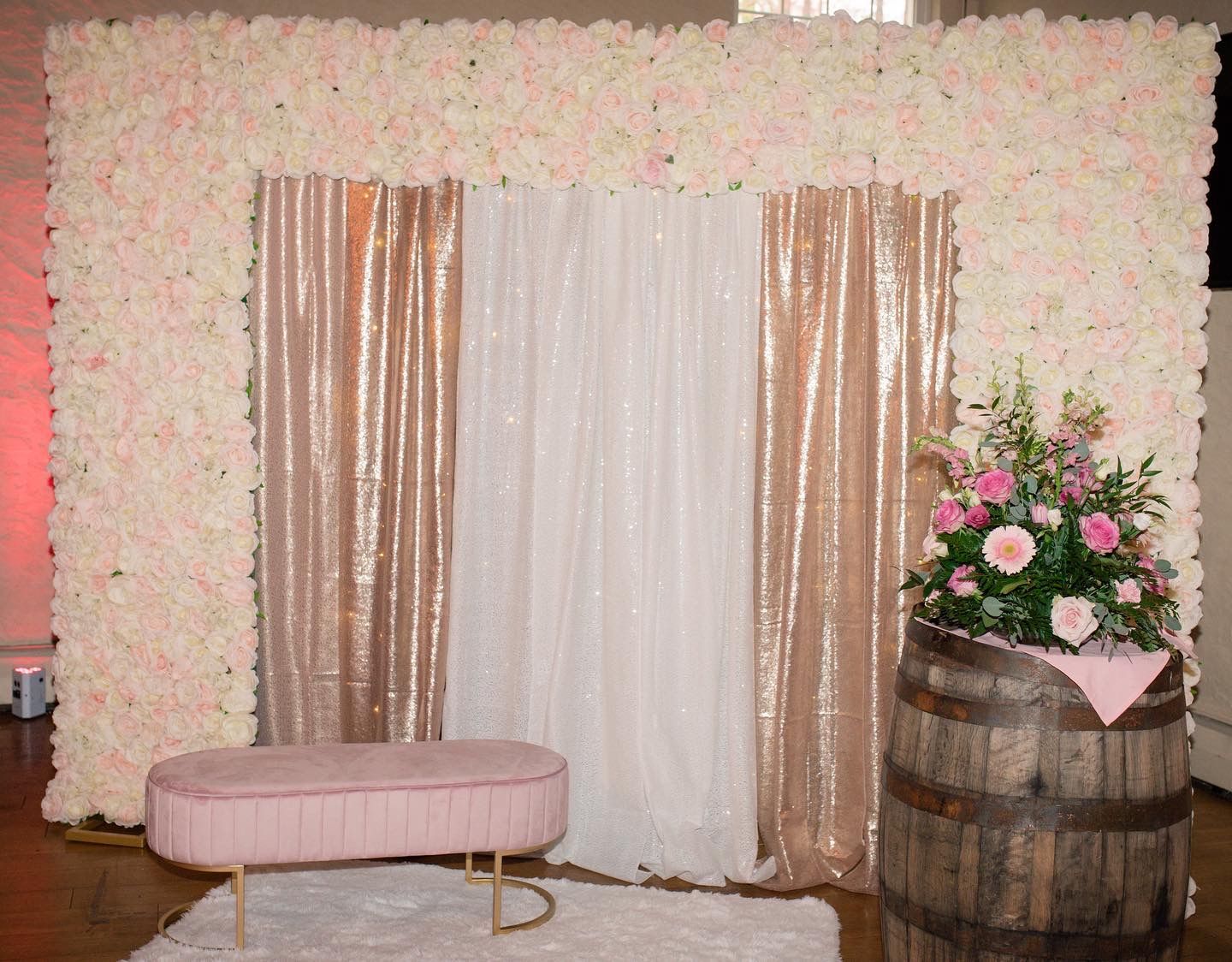 Floral backdrop with gold curtains, bench, and barrel of flowers.