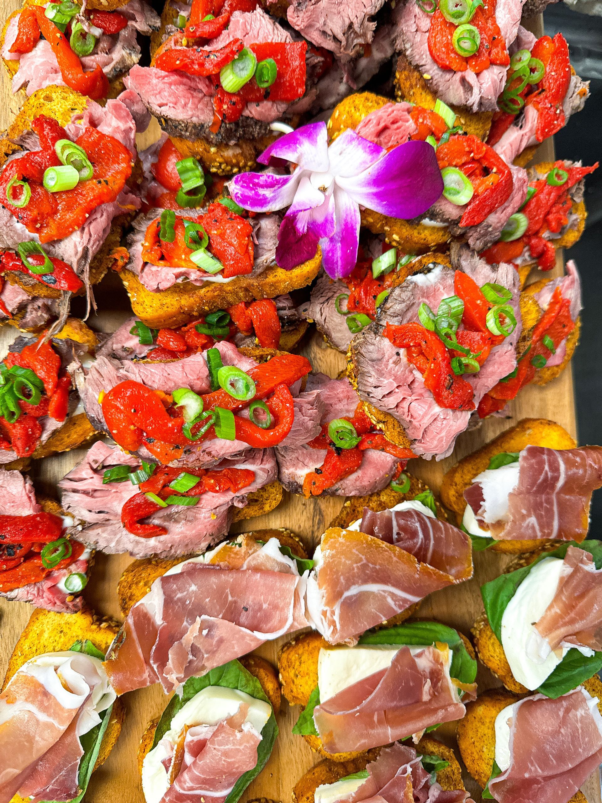 Appetizers on toast, topped with roast beef and peppers, plus prosciutto, mozzarella, and basil.