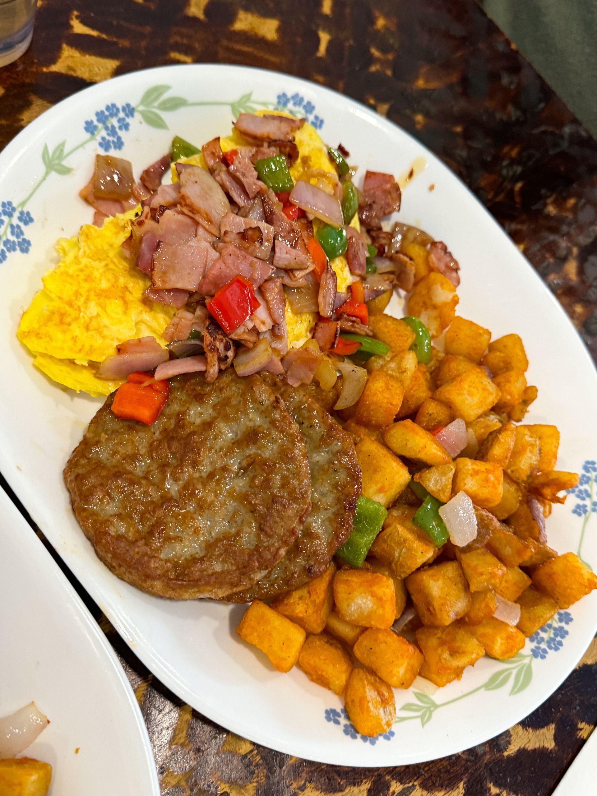 Breakfast plate with omelet, ham, sausage patties, and seasoned potatoes.