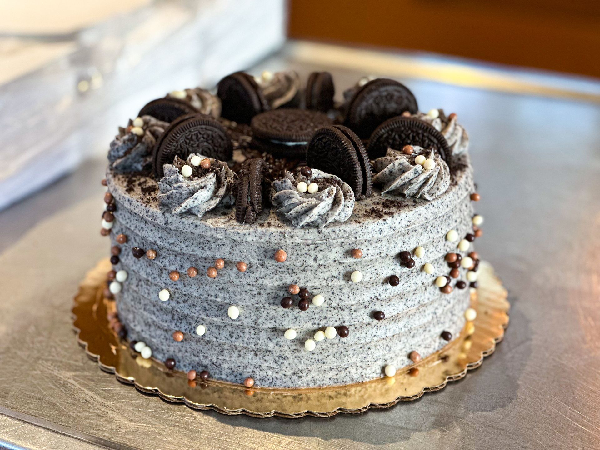 Oreo cake with gray frosting, decorated with cookies and sprinkles, on a gold cake board.