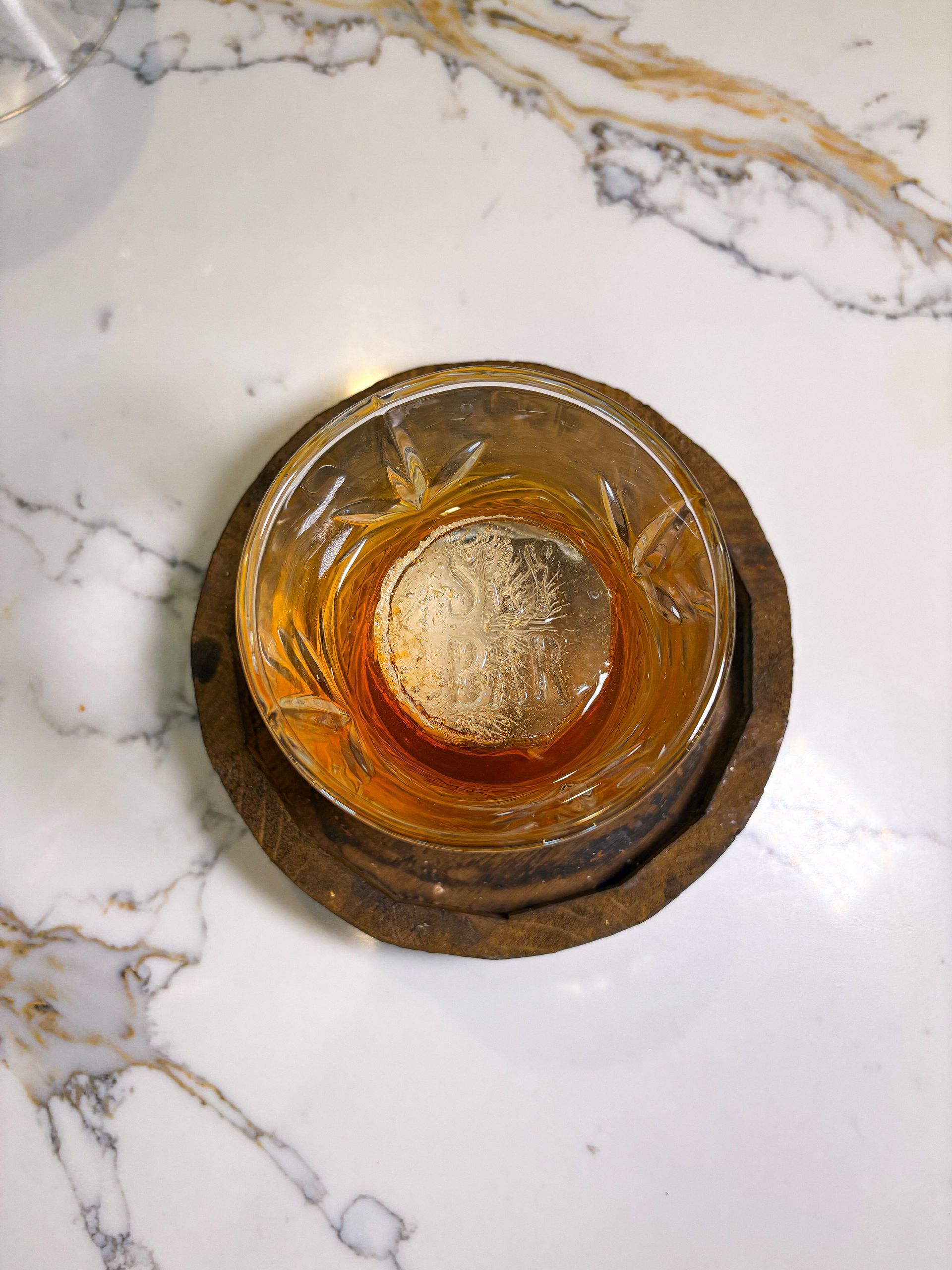 Glass bowl of amber liquid on a wooden coaster, set on a marble surface.