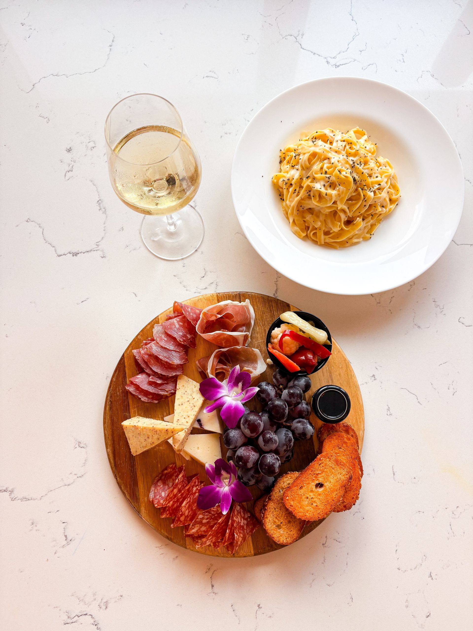 Charcuterie board with salami, cheese, grapes, and crackers, pasta, and wine.