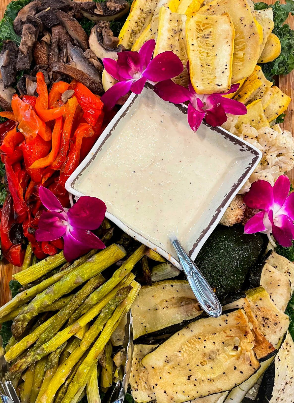Grilled vegetables platter with dip, colorful arrangement, garnished with orchids.