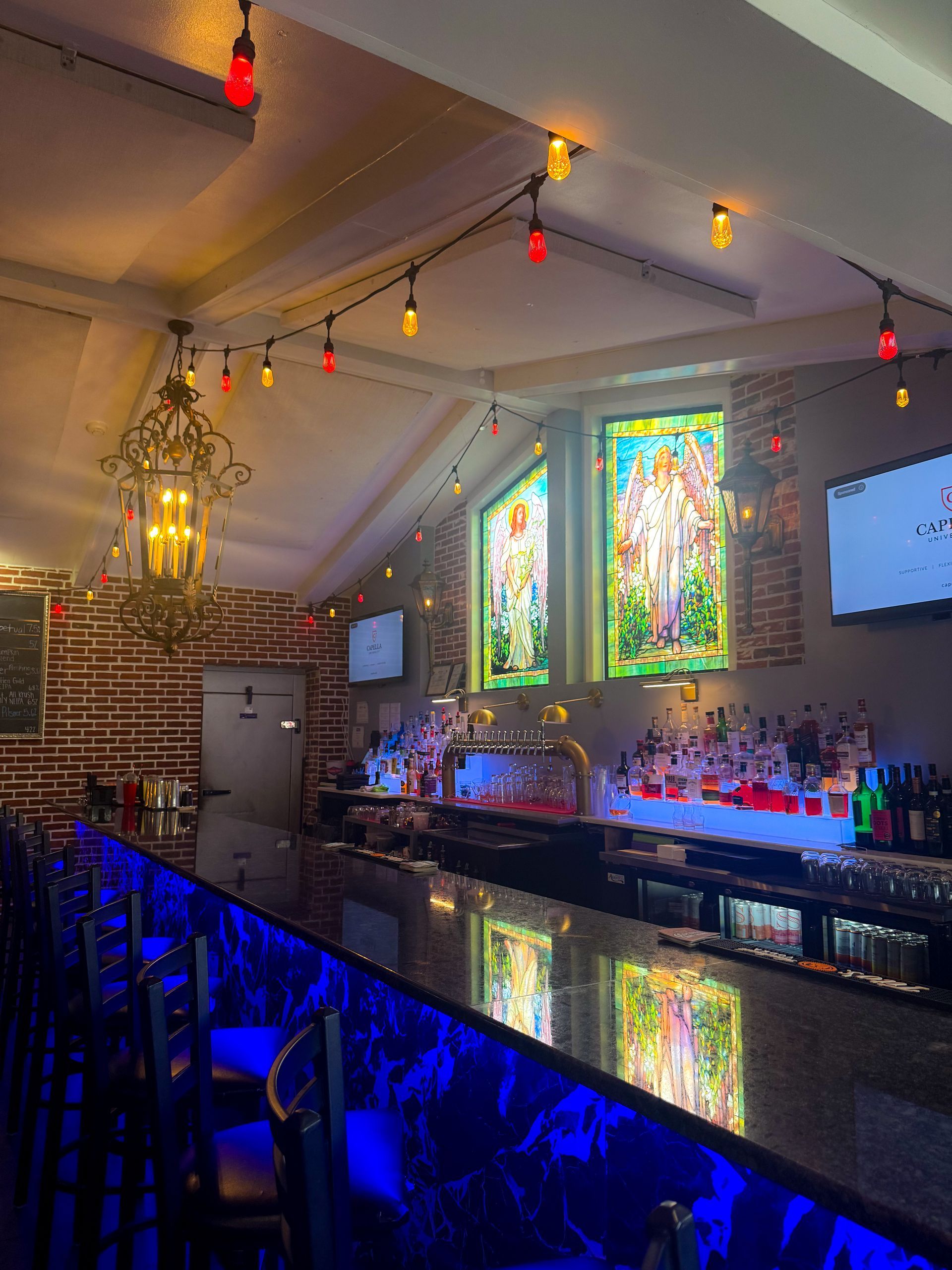 Bar interior with a dark bar, colorful lights, and stained glass windows.