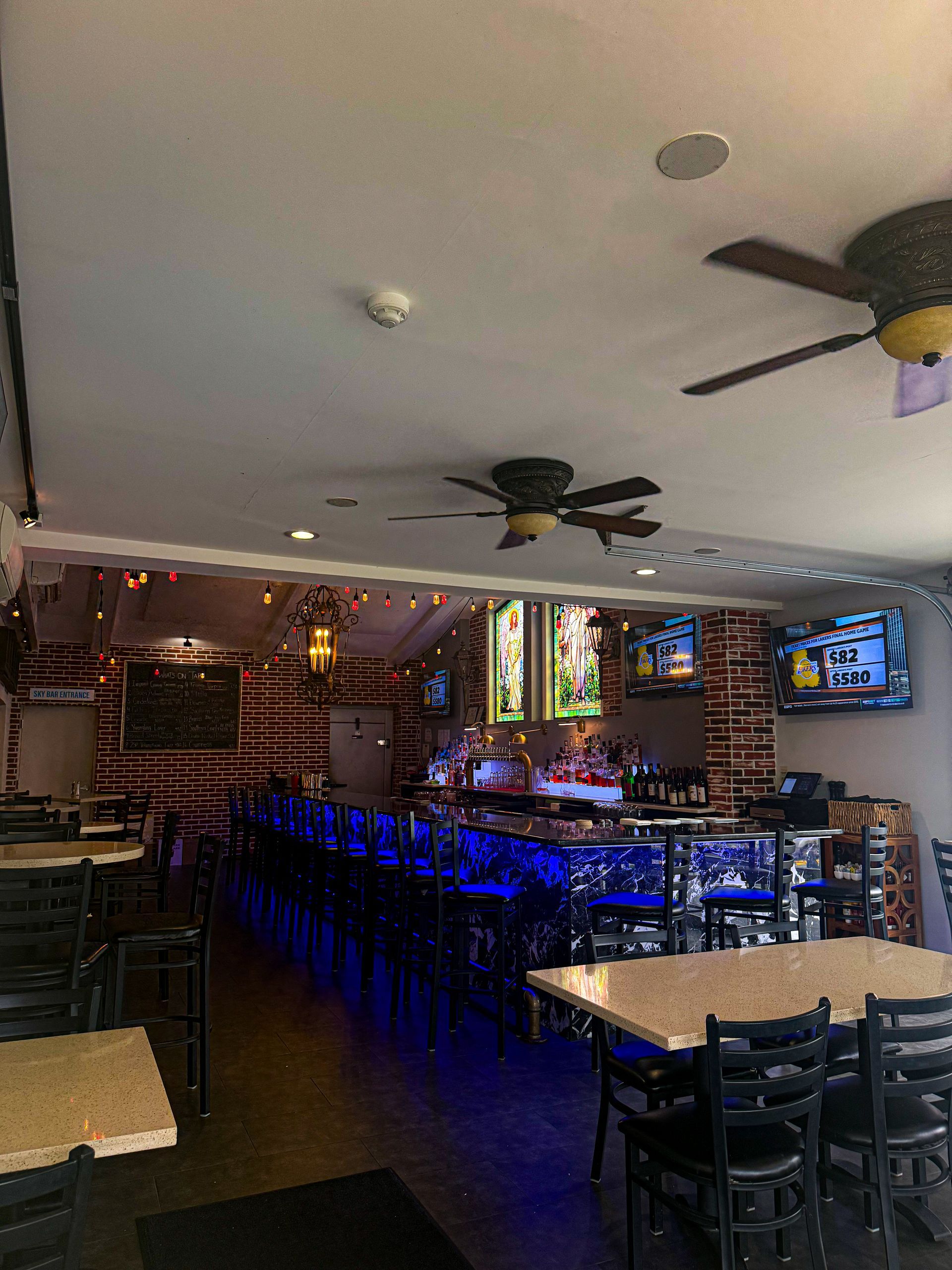 Interior of a bar with tables, chairs, and a long bar with blue underlighting. TVs are visible.