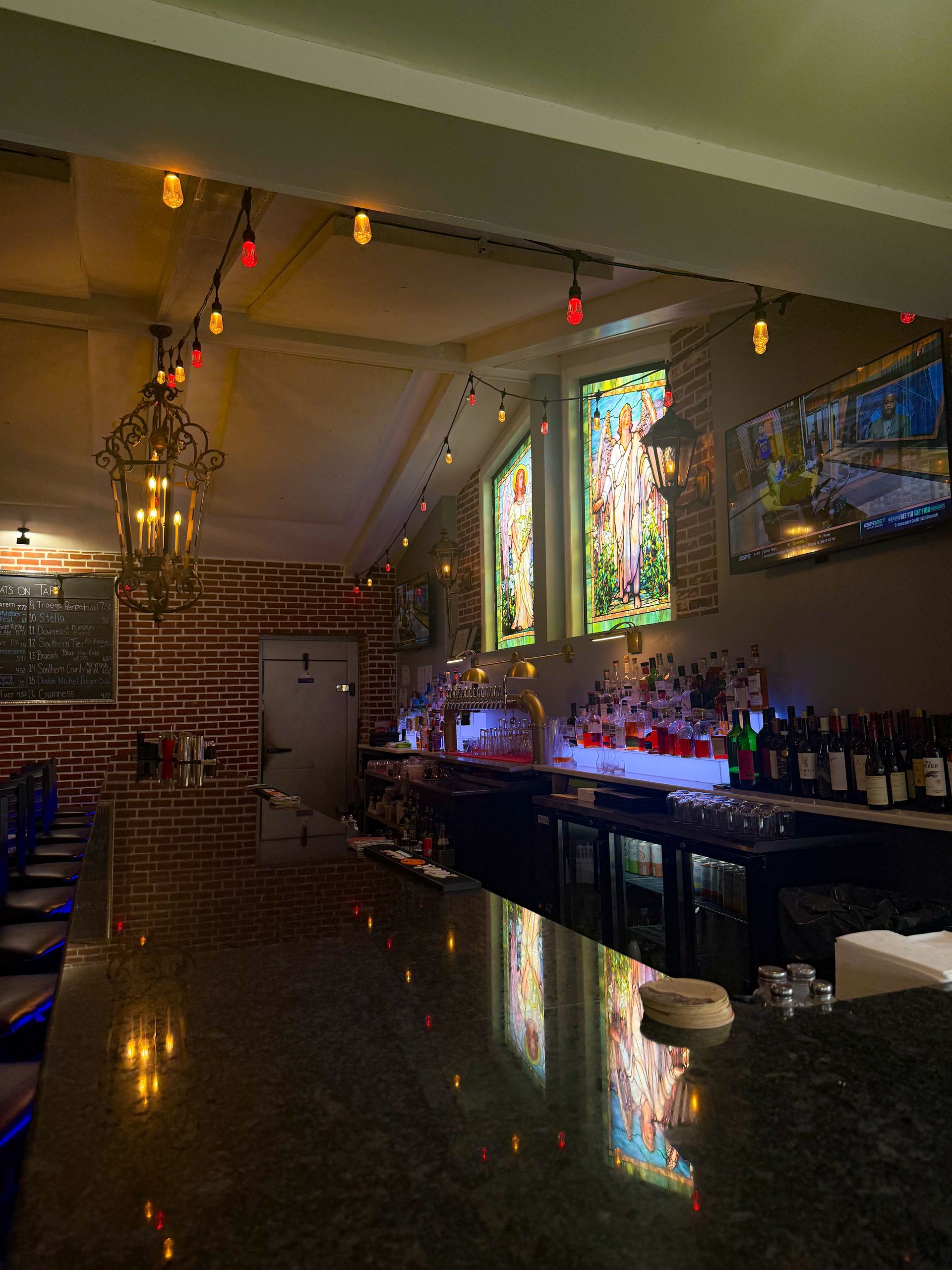 Bar interior with a dark countertop, stained glass windows, and string lights.