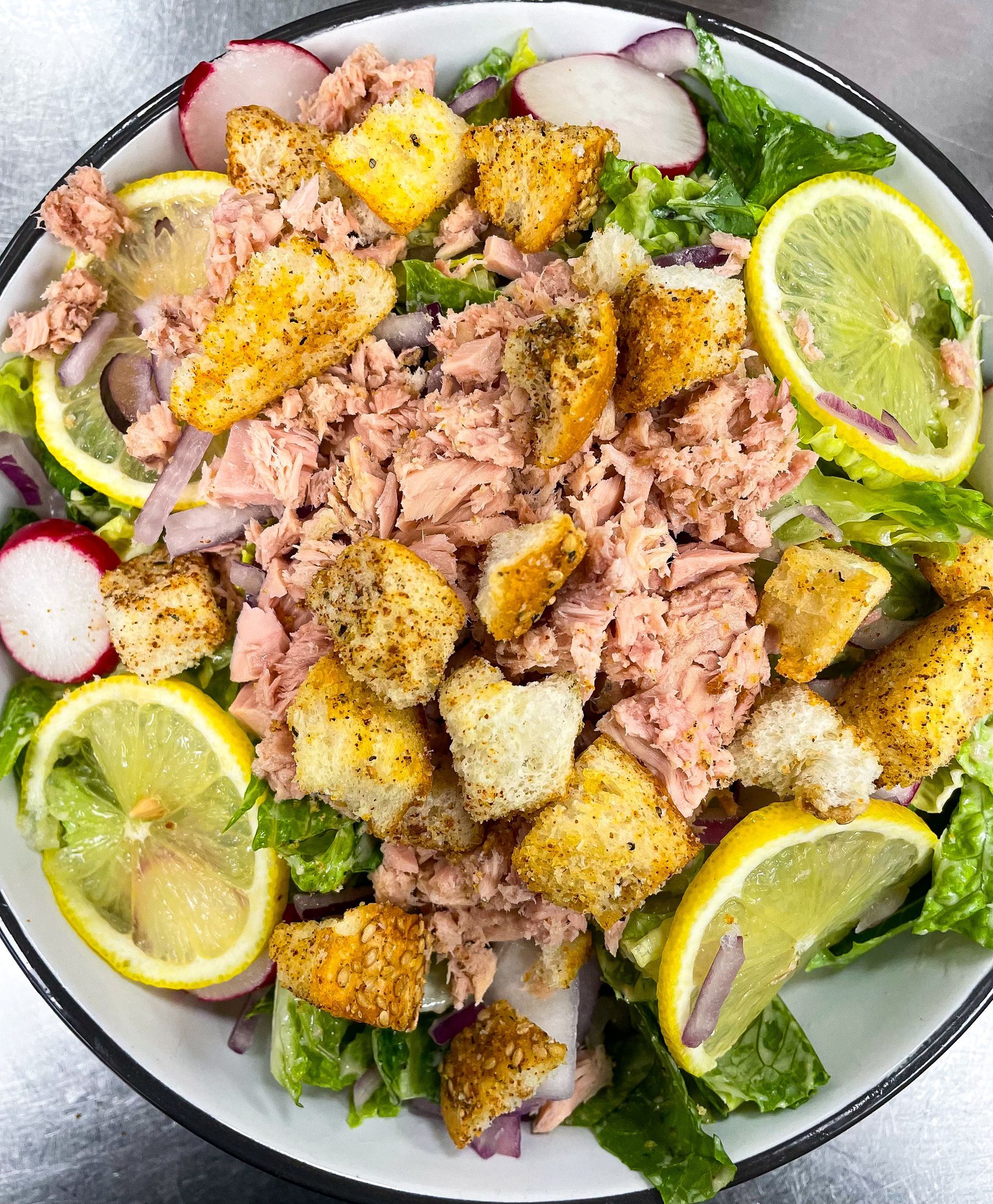 Tuna salad in a bowl with lemon slices, croutons, red onion, and radishes.