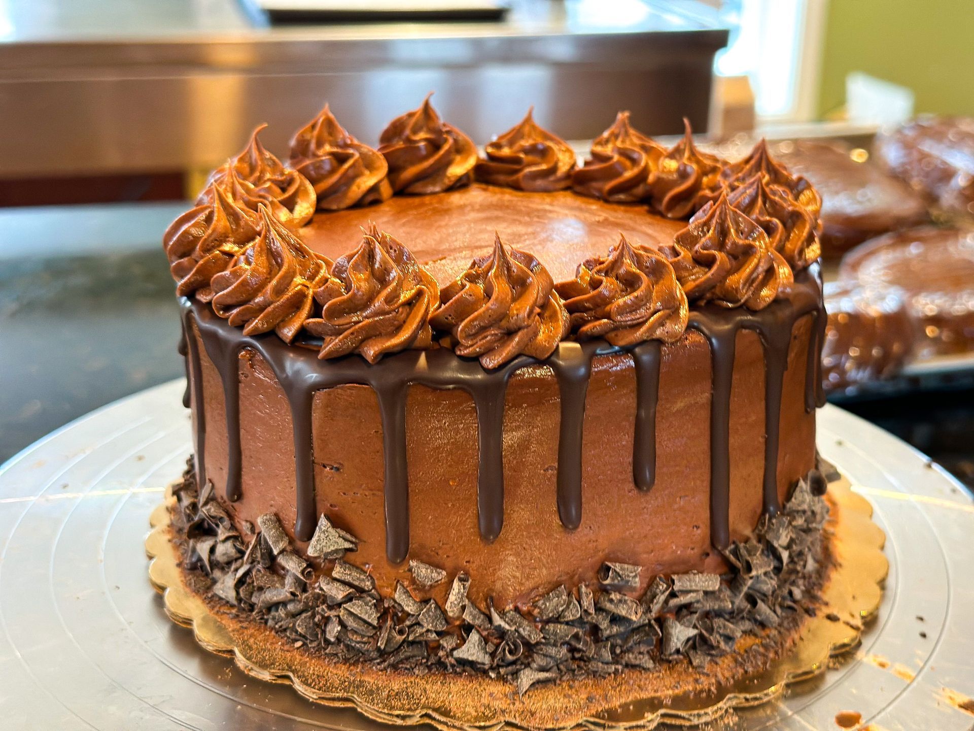 Chocolate cake with chocolate frosting, piped rosettes, and chocolate drip, on a gold base.