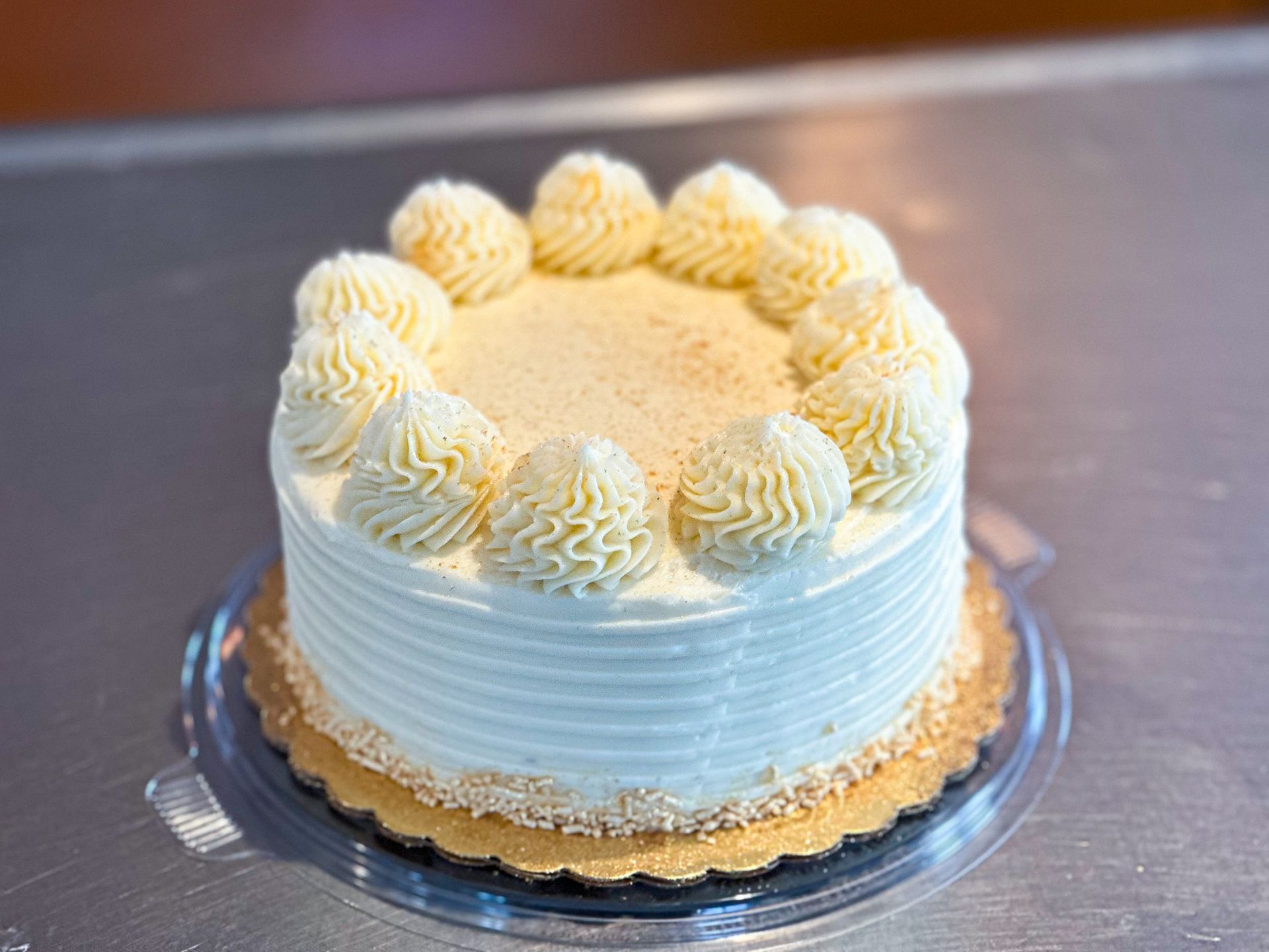 Small round cake with white frosting and decorative swirls, on a gold cardboard base.