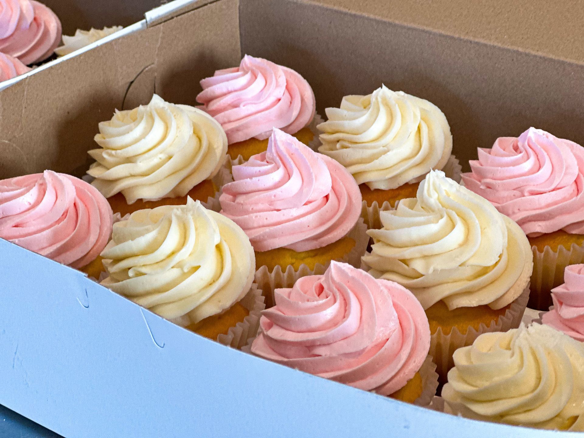 Cupcakes in box with pink and cream-colored frosting, arranged in rows.