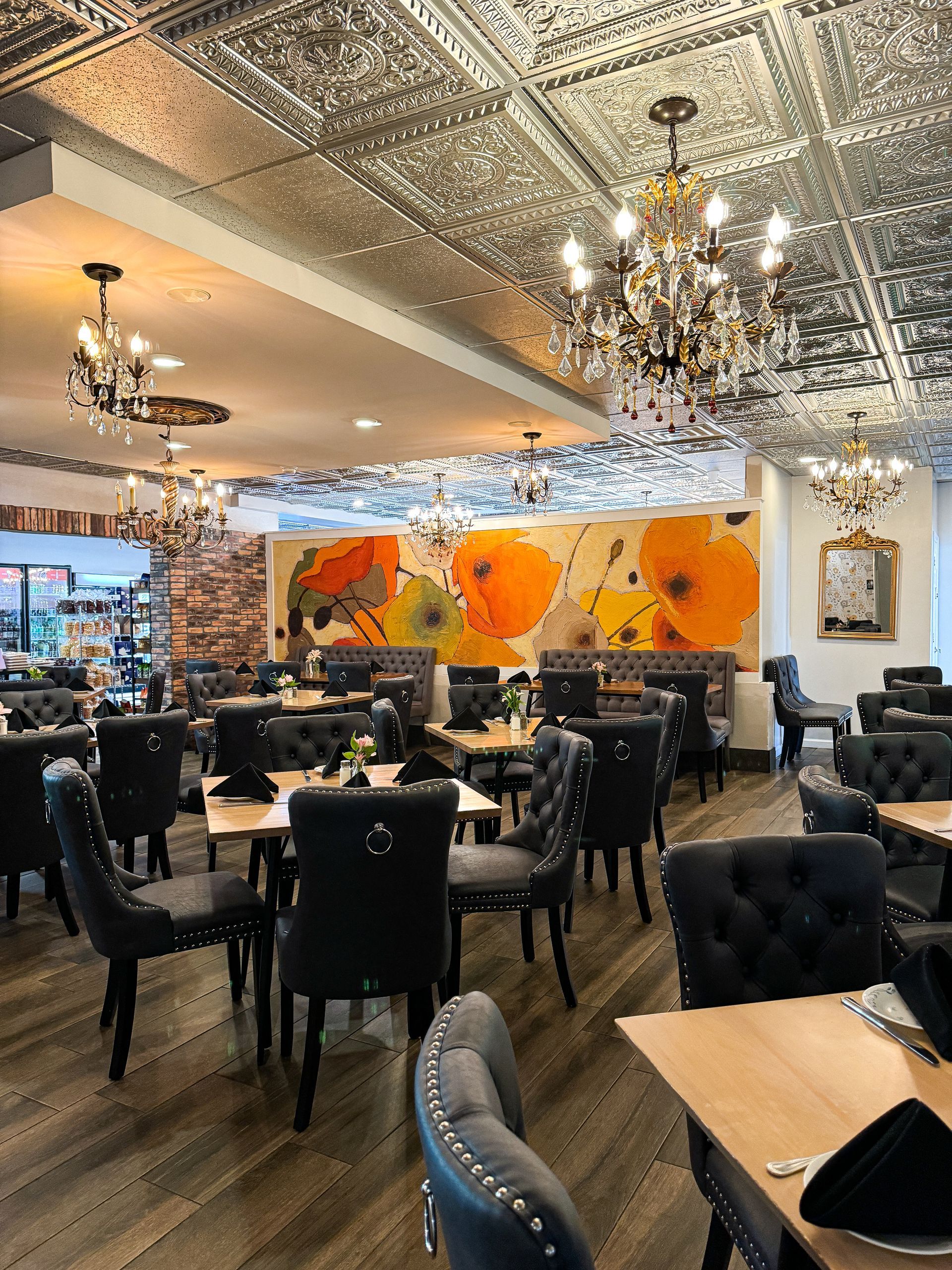 Restaurant interior with tables, chairs, chandeliers, and floral artwork on the wall.