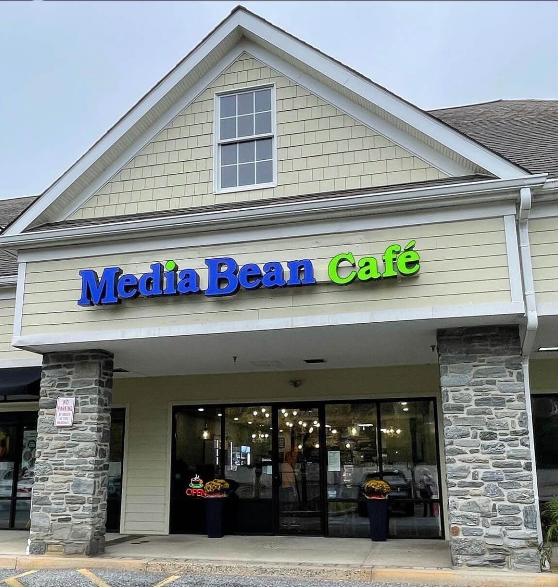 Media Bean Café storefront with blue and green sign, light tan siding, and stone accents.