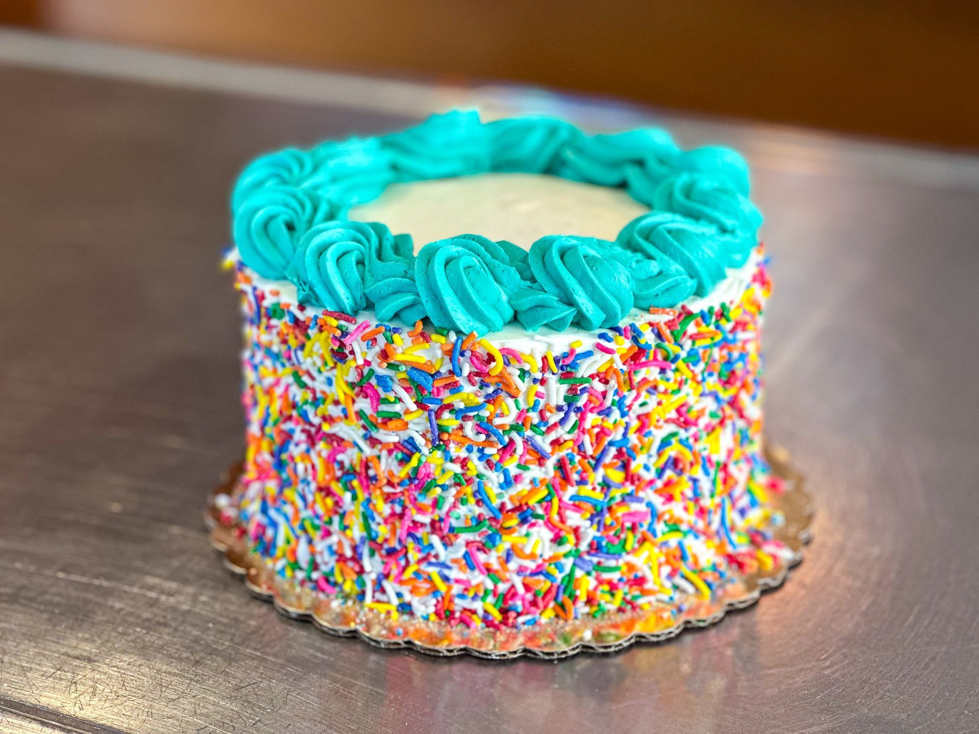 Small cake with rainbow sprinkles and teal frosting.