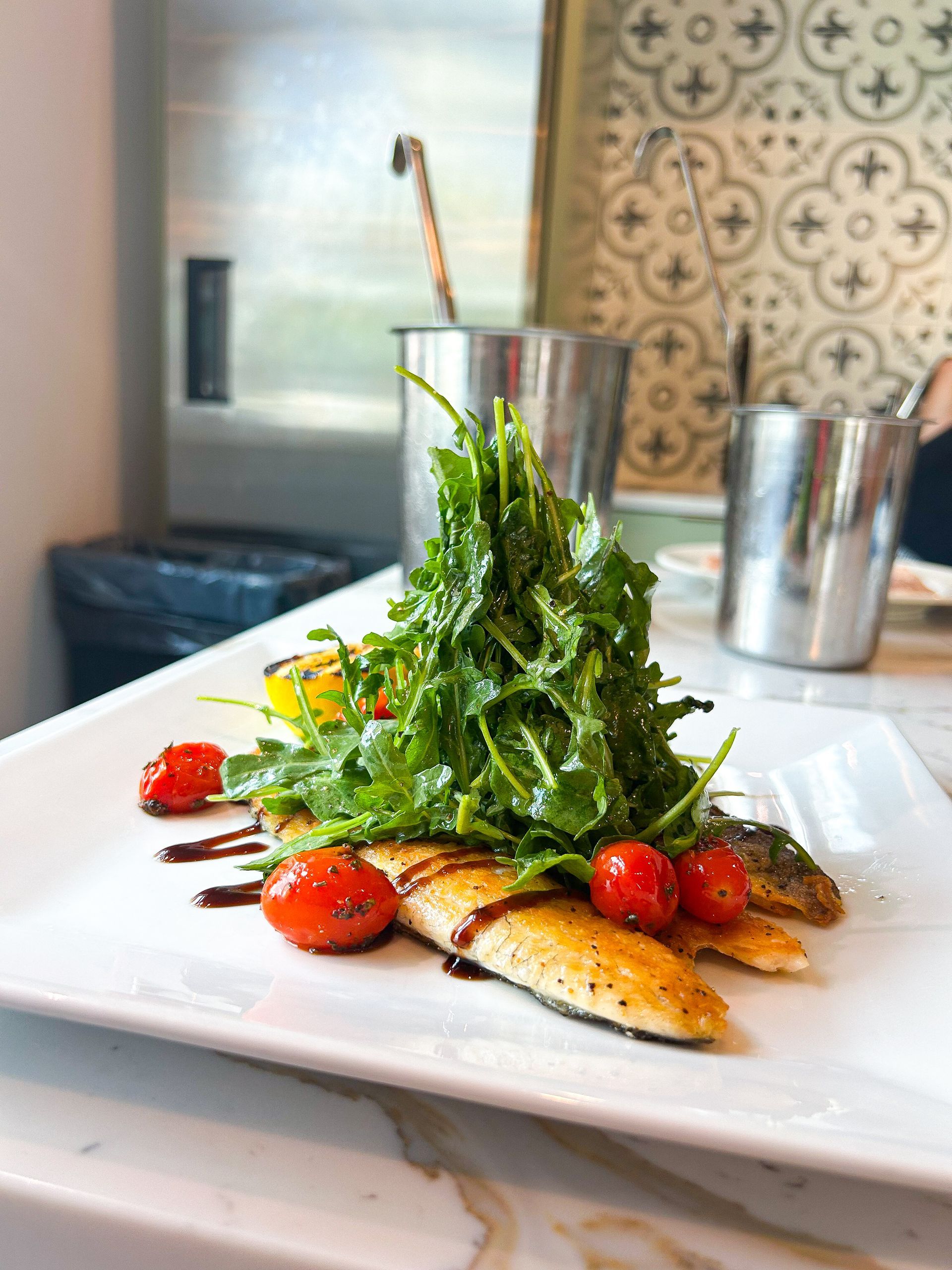 Grilled fish fillets with arugula, tomatoes, and balsamic glaze on a white plate.