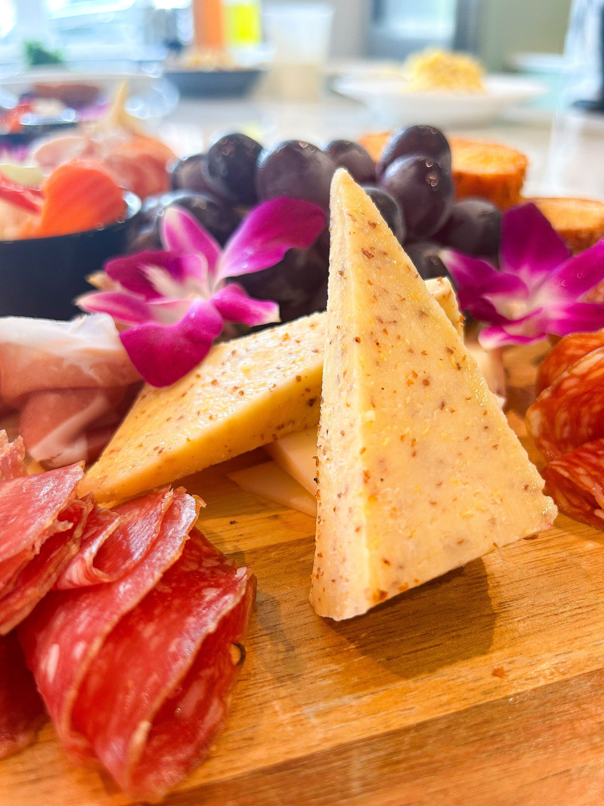 Charcuterie board with cheese, grapes, salami, and flowers.