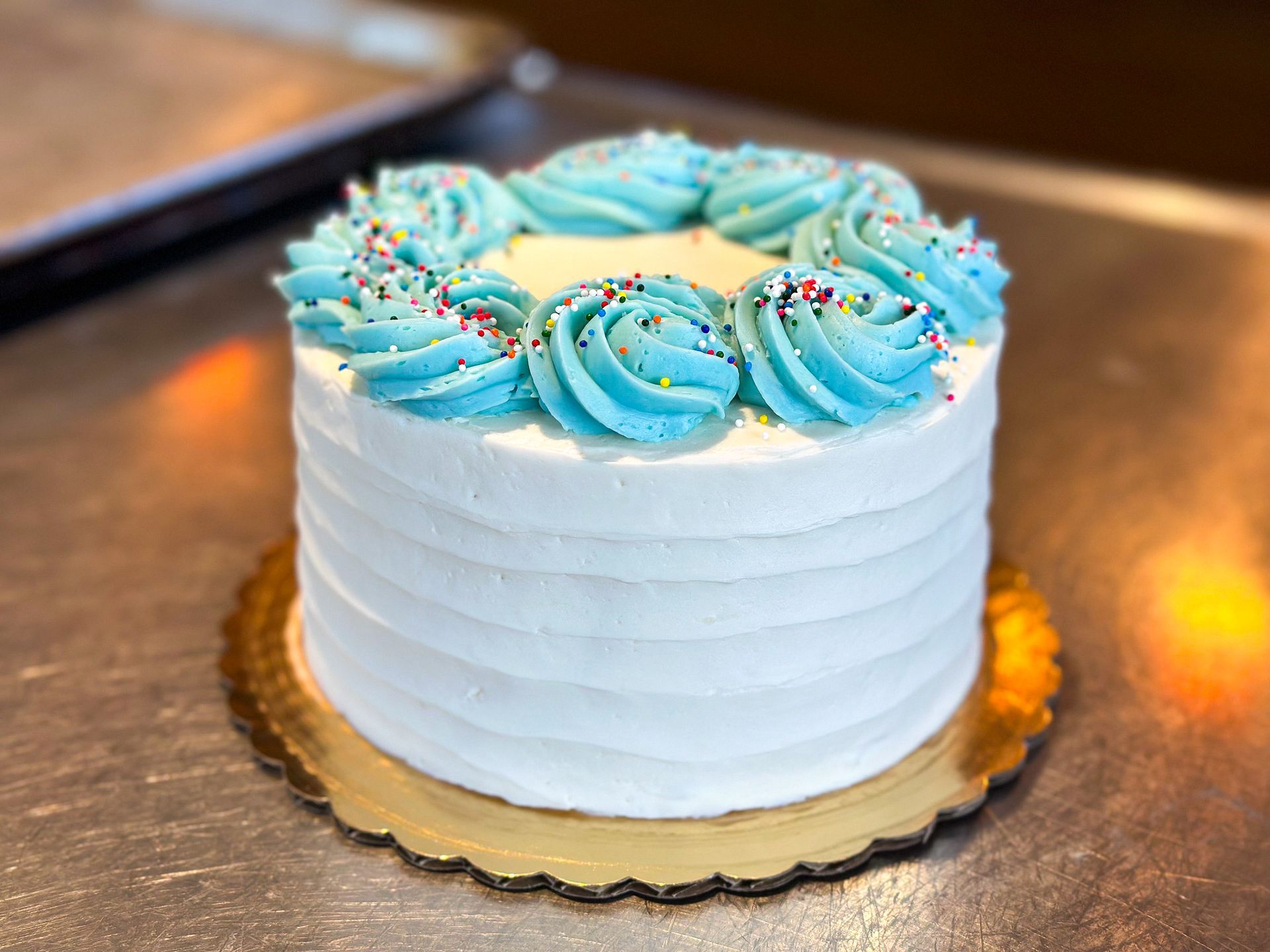 Small white cake with blue frosting swirls and sprinkles on a gold doily.
