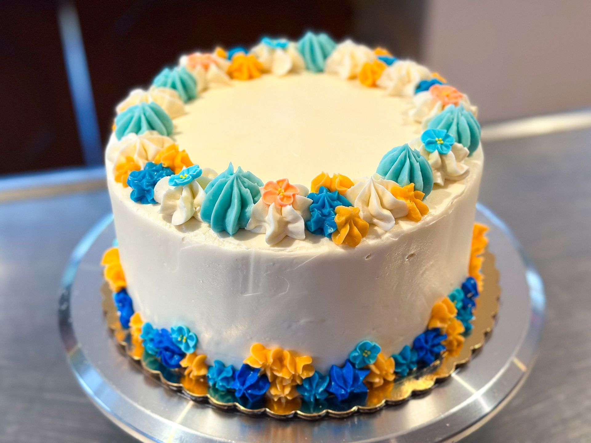 White frosted cake decorated with blue, orange, and white buttercream rosettes.