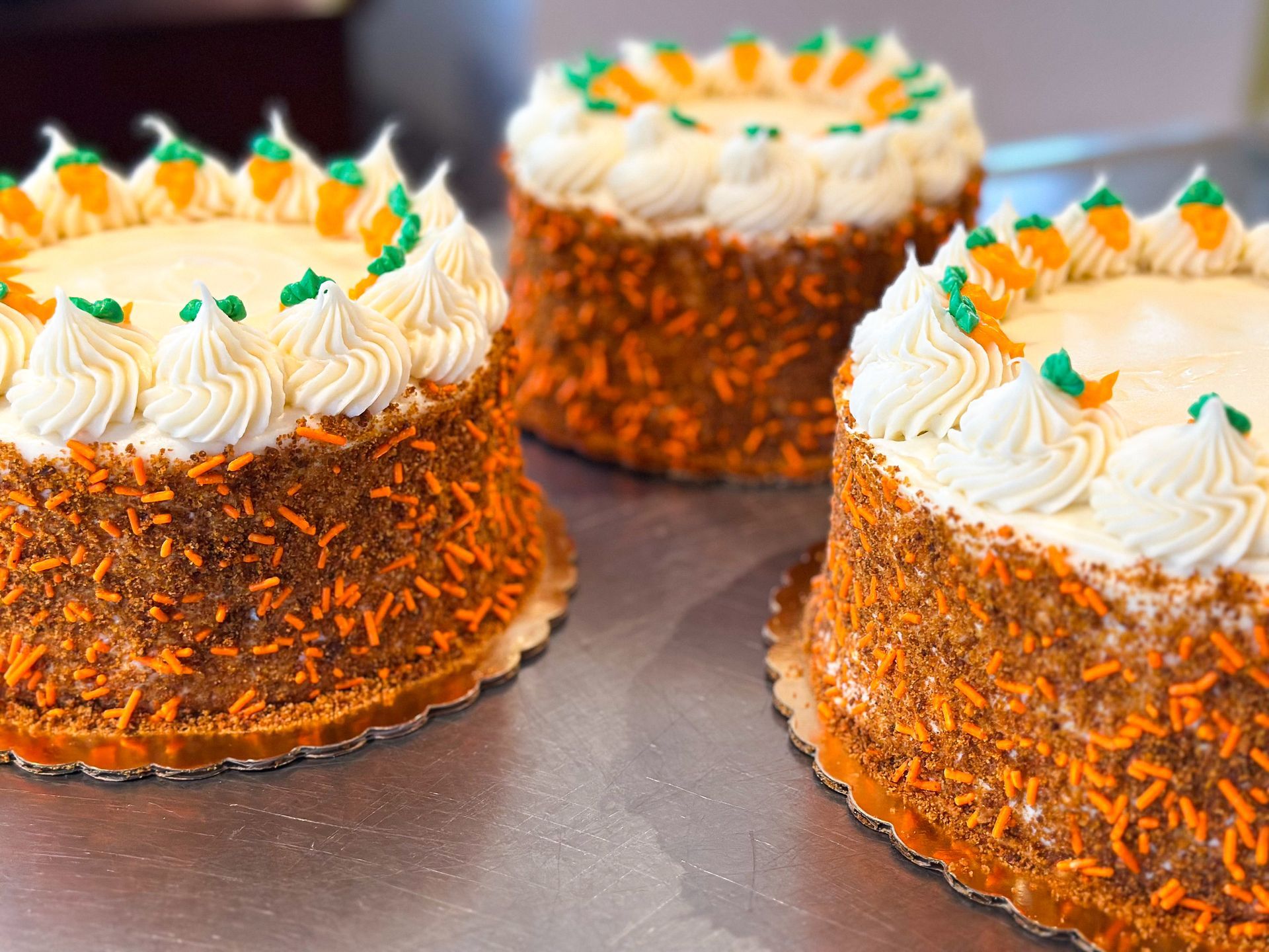 Three carrot cakes with orange sprinkles and white frosting, decorated with frosting carrots.