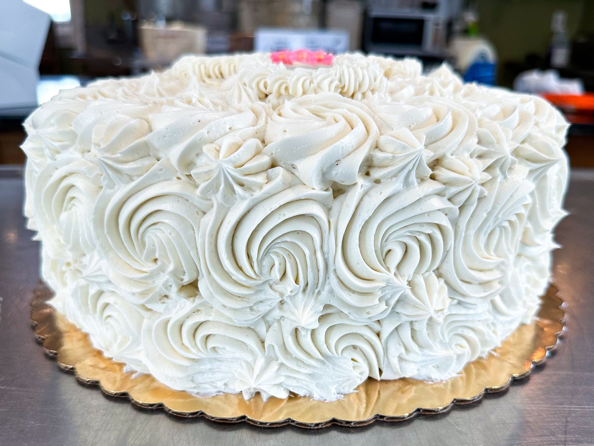 Cake with white frosting piped in rose patterns on a gold cake board.