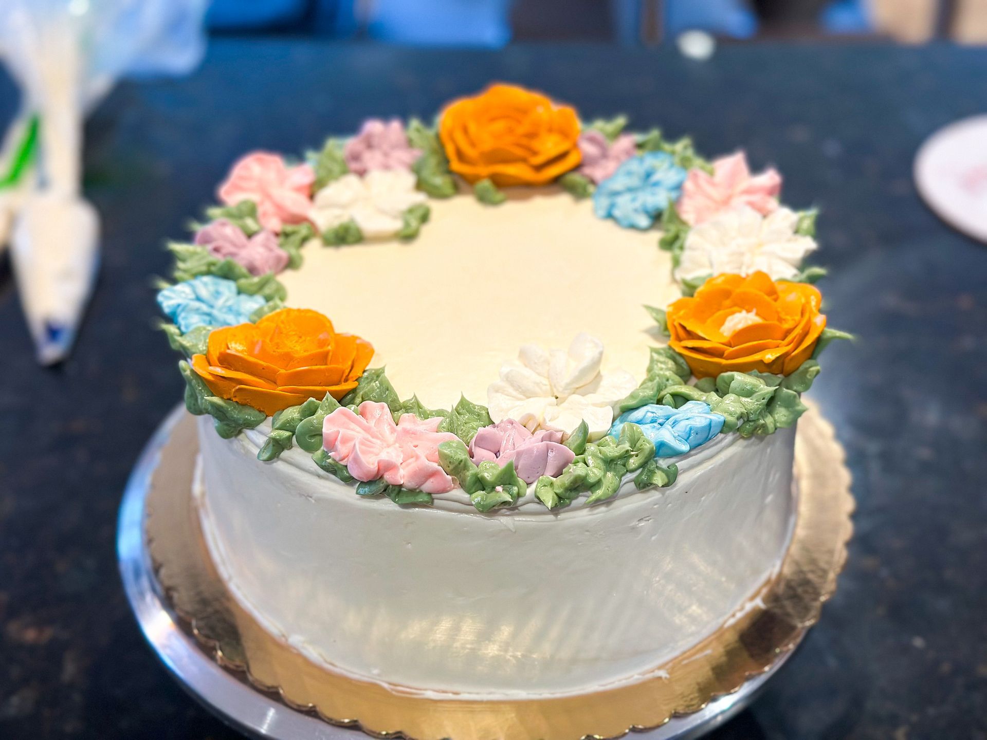 Cake decorated with frosting flowers in orange, pink, blue, and white; on a gold cake stand.