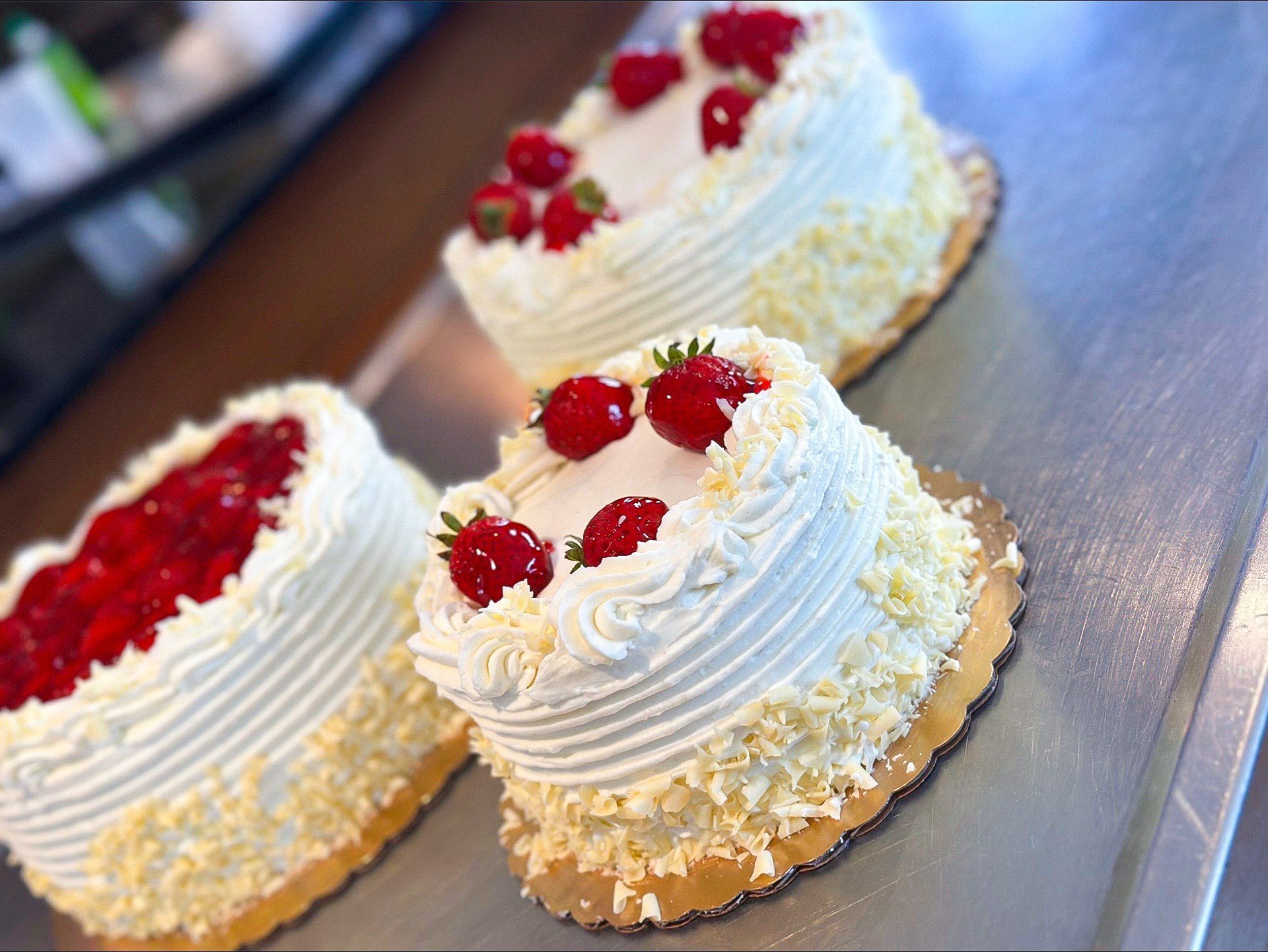 Three small white cakes topped with strawberries, sitting on a metallic surface.