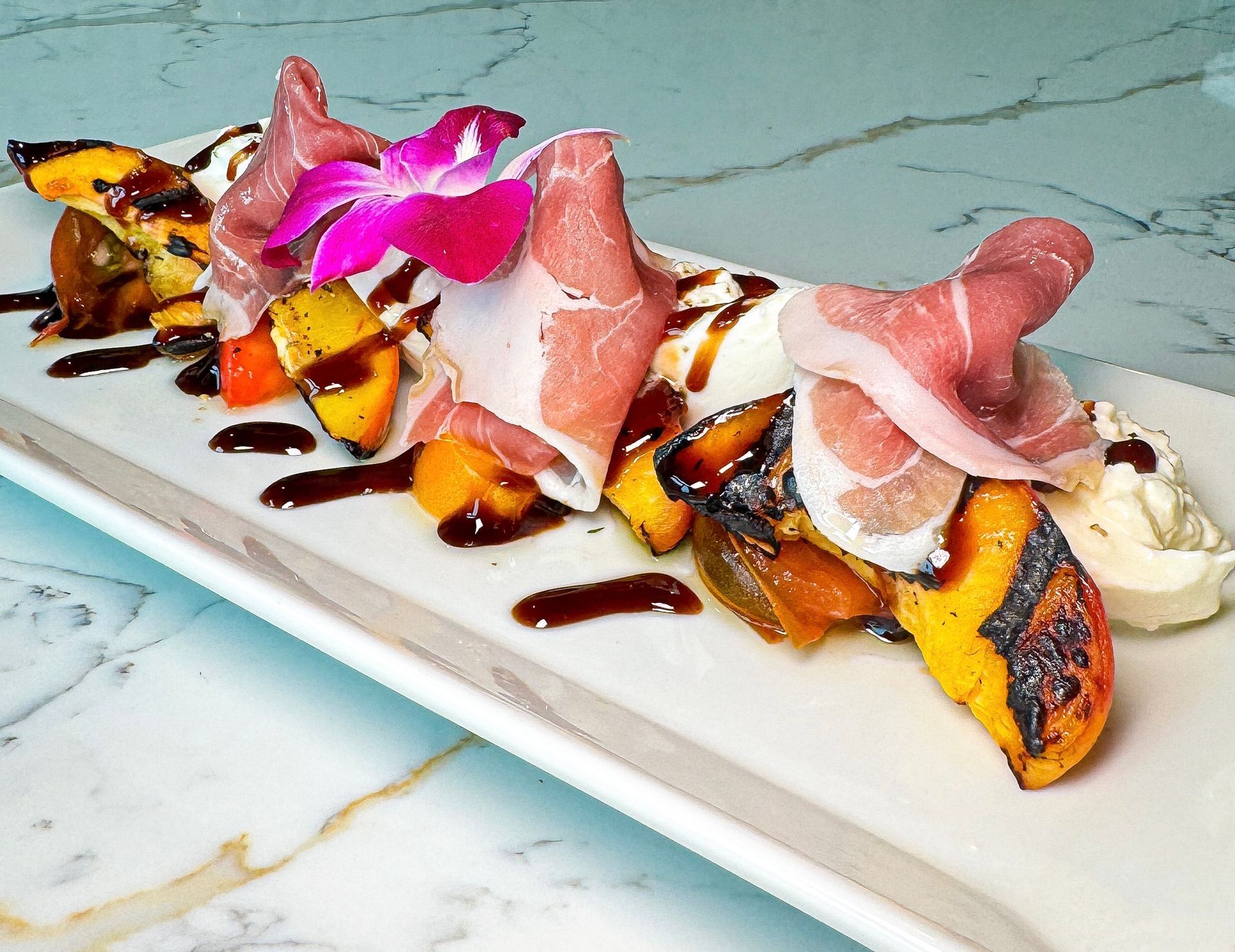 Grilled peach and prosciutto appetizer with balsamic glaze and cream.
