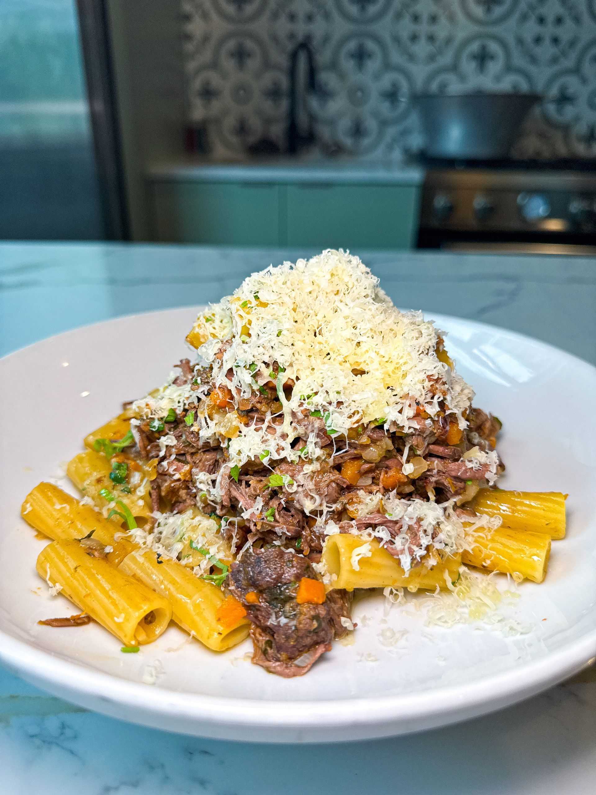 Pasta dish with meat ragu and grated cheese, on a white plate.