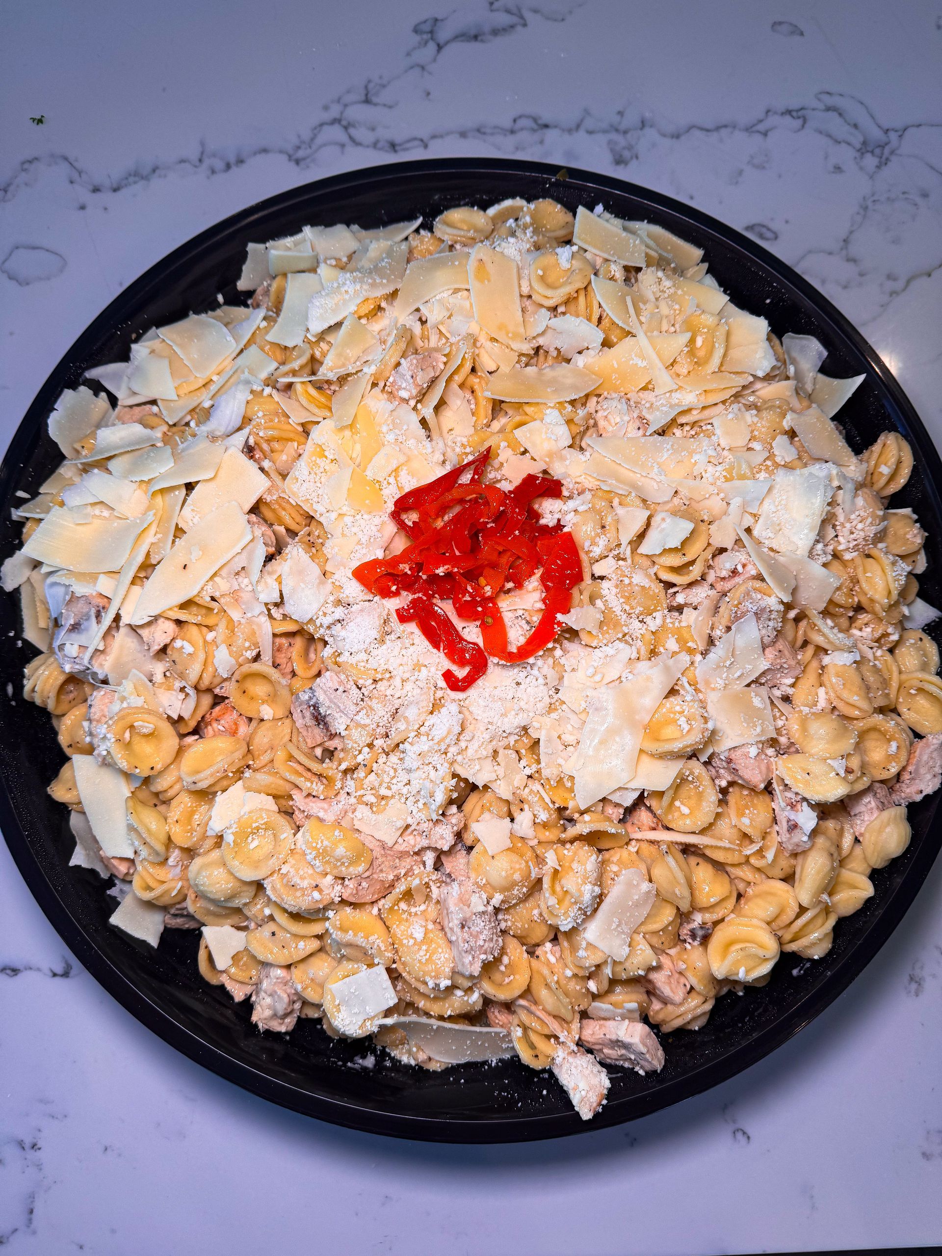 Overhead view of a black bowl filled with a layered food dish, topped with flakes and a red condiment.