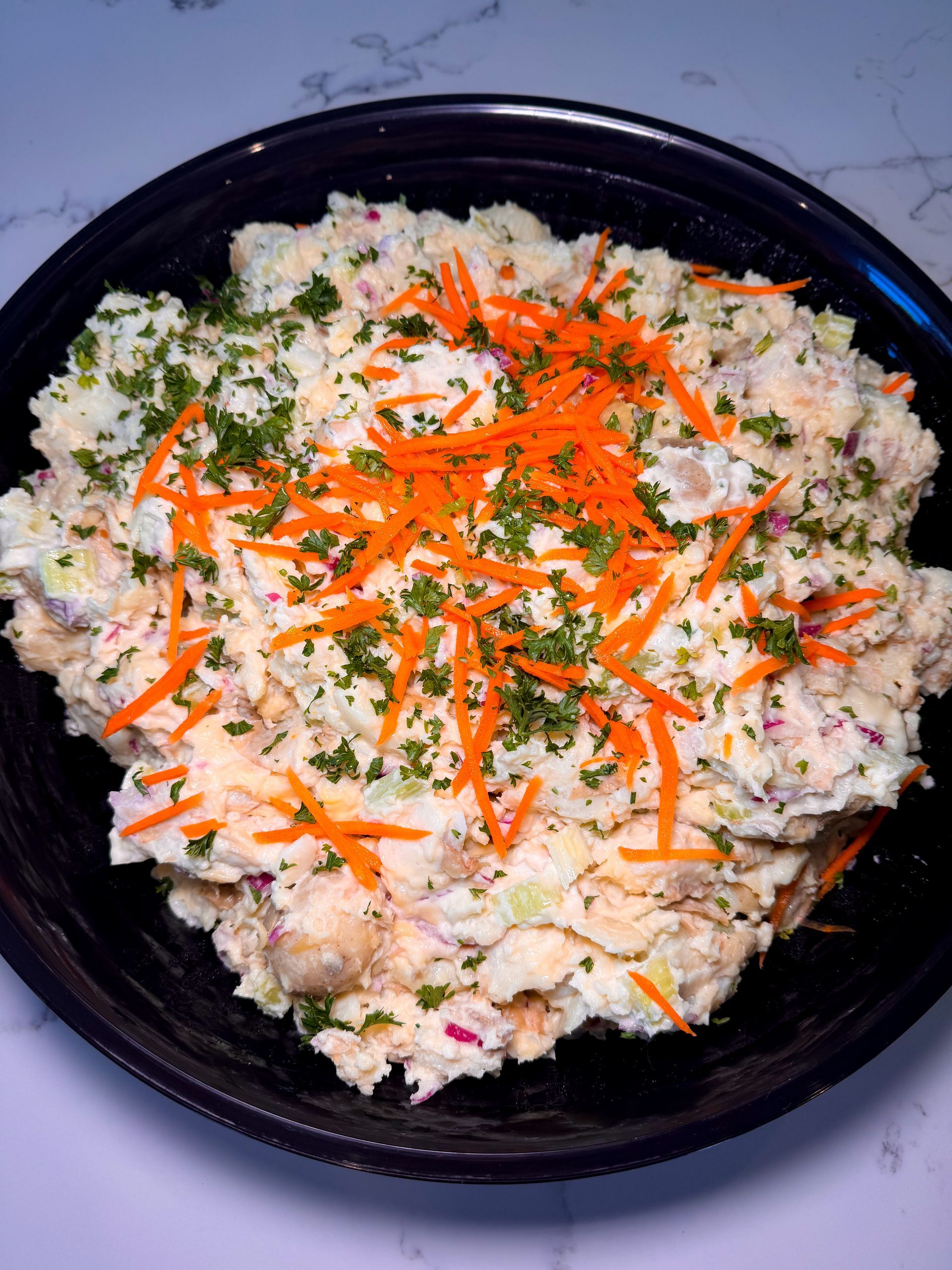 Potato salad in a black bowl, topped with shredded carrots and parsley.