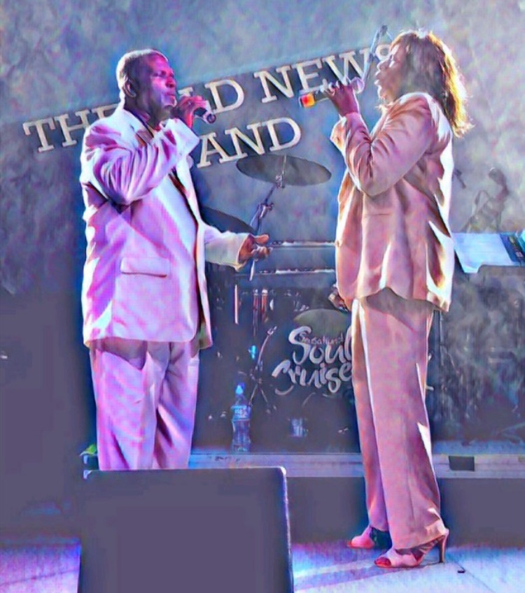 Two singers in pink suits perform onstage, facing each other with microphones.