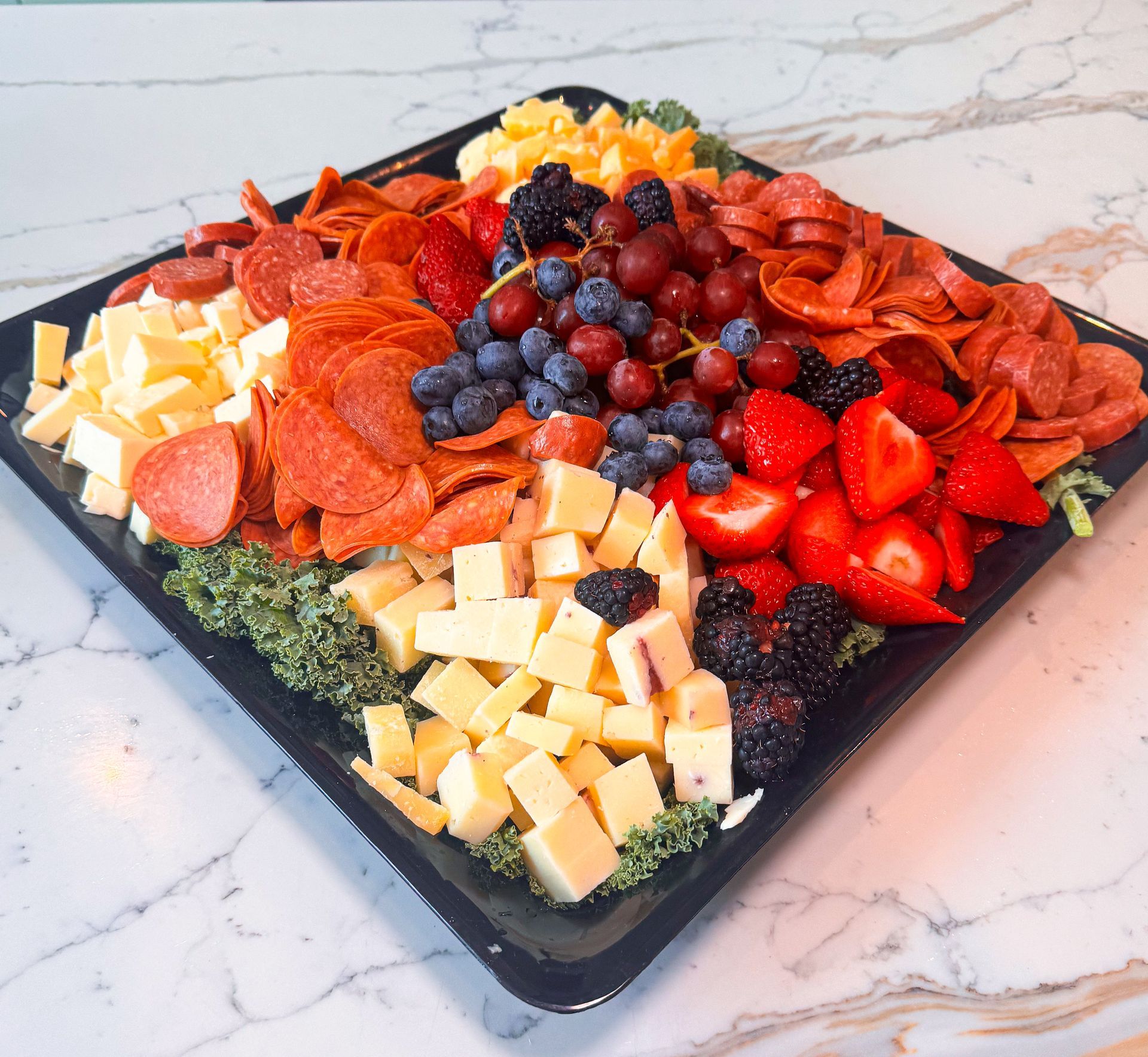 Charcuterie platter: pepperoni, cheese cubes, berries, grapes, sausage, on a black square tray.