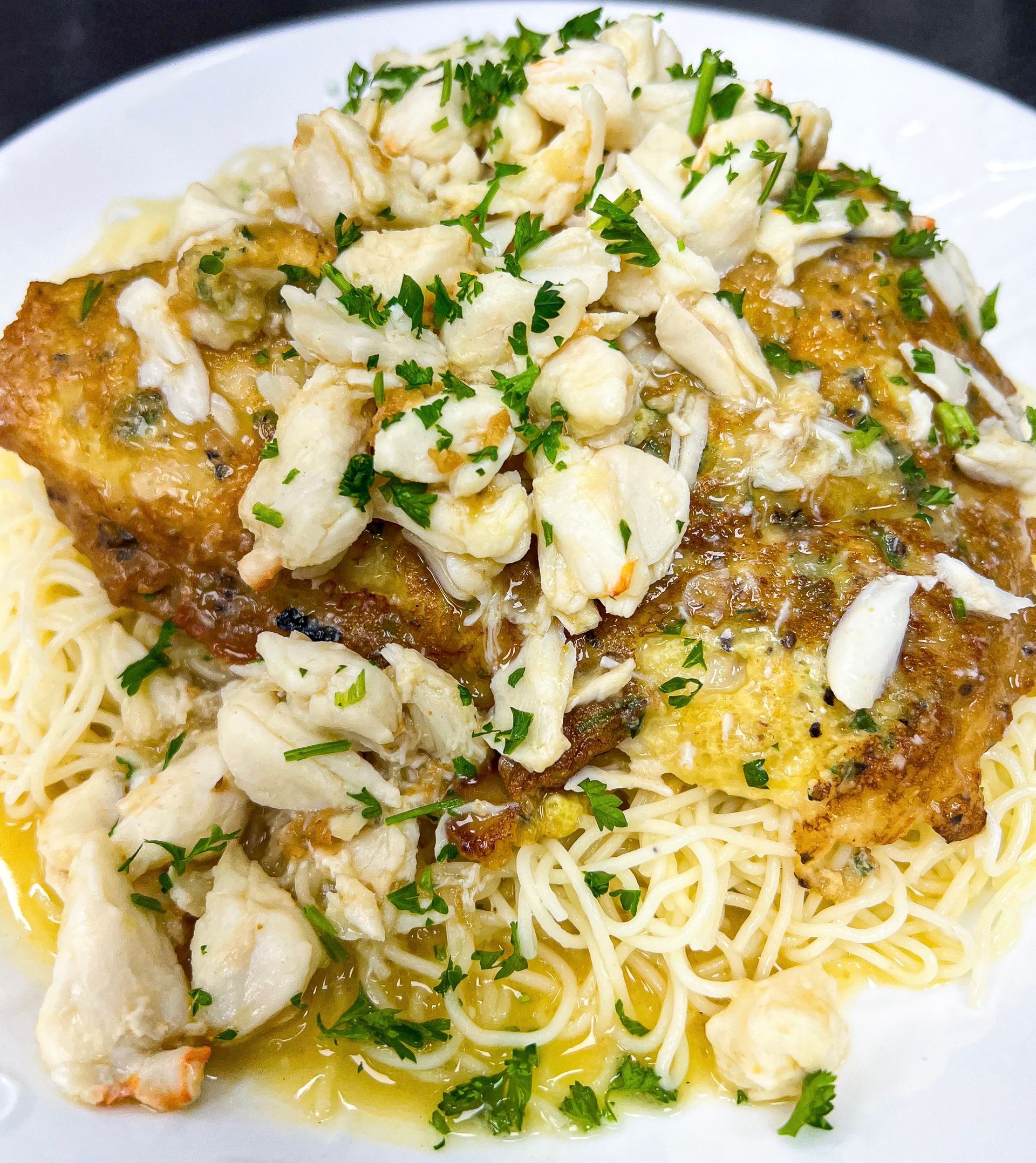 Pasta dish: golden-brown fried fish topped with crab meat and parsley, over spaghetti.