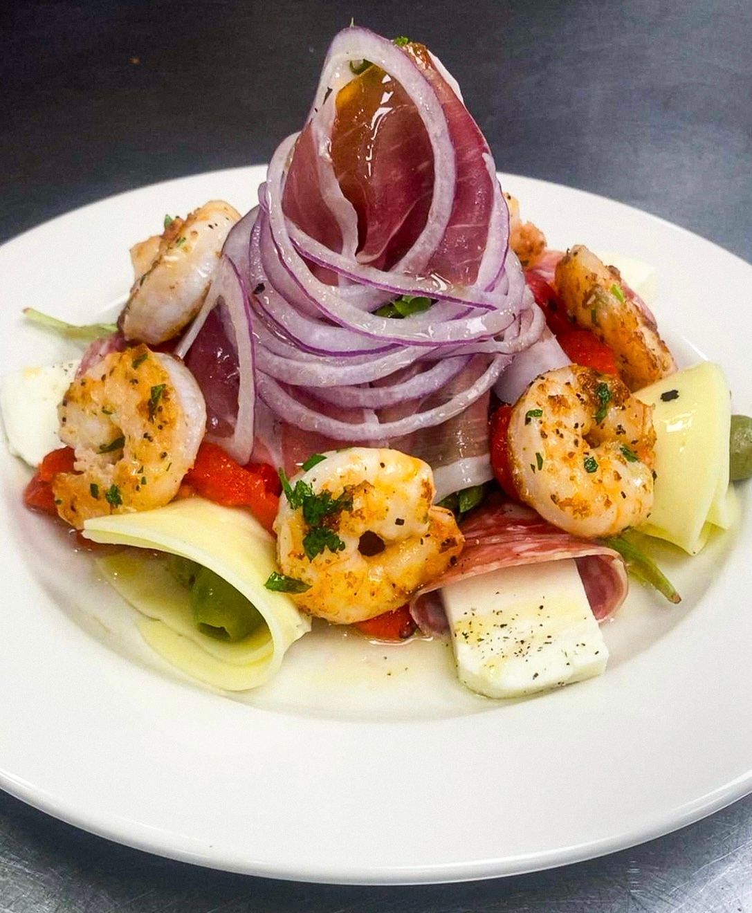 Salad with shrimp, prosciutto, red onion, artichoke hearts, cheese, and salami on a white plate.