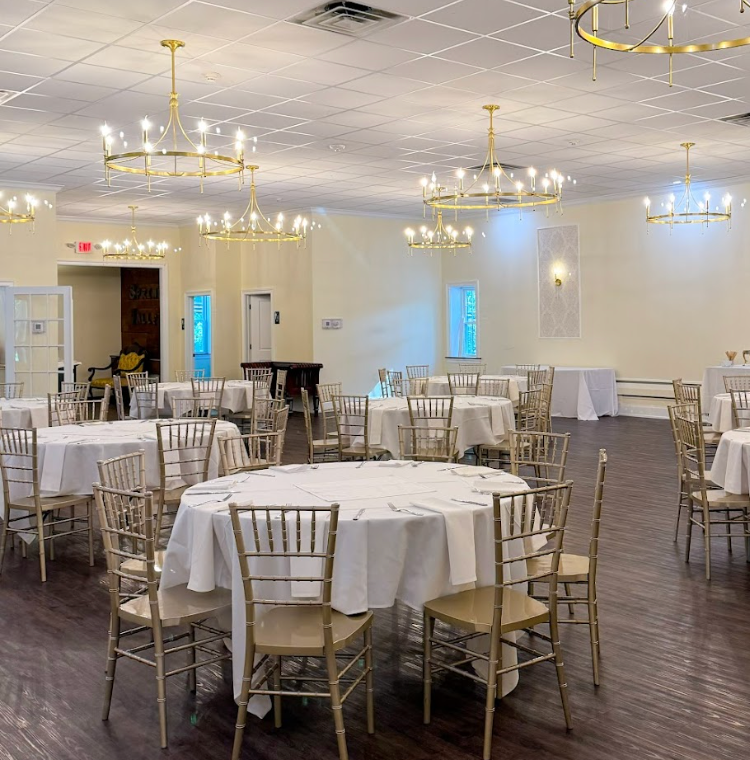 Empty banquet hall with round tables, chairs, and golden chandeliers.