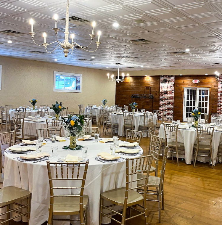 Banquet hall with round tables set for a formal event; gold chairs, white linens, floral centerpieces.