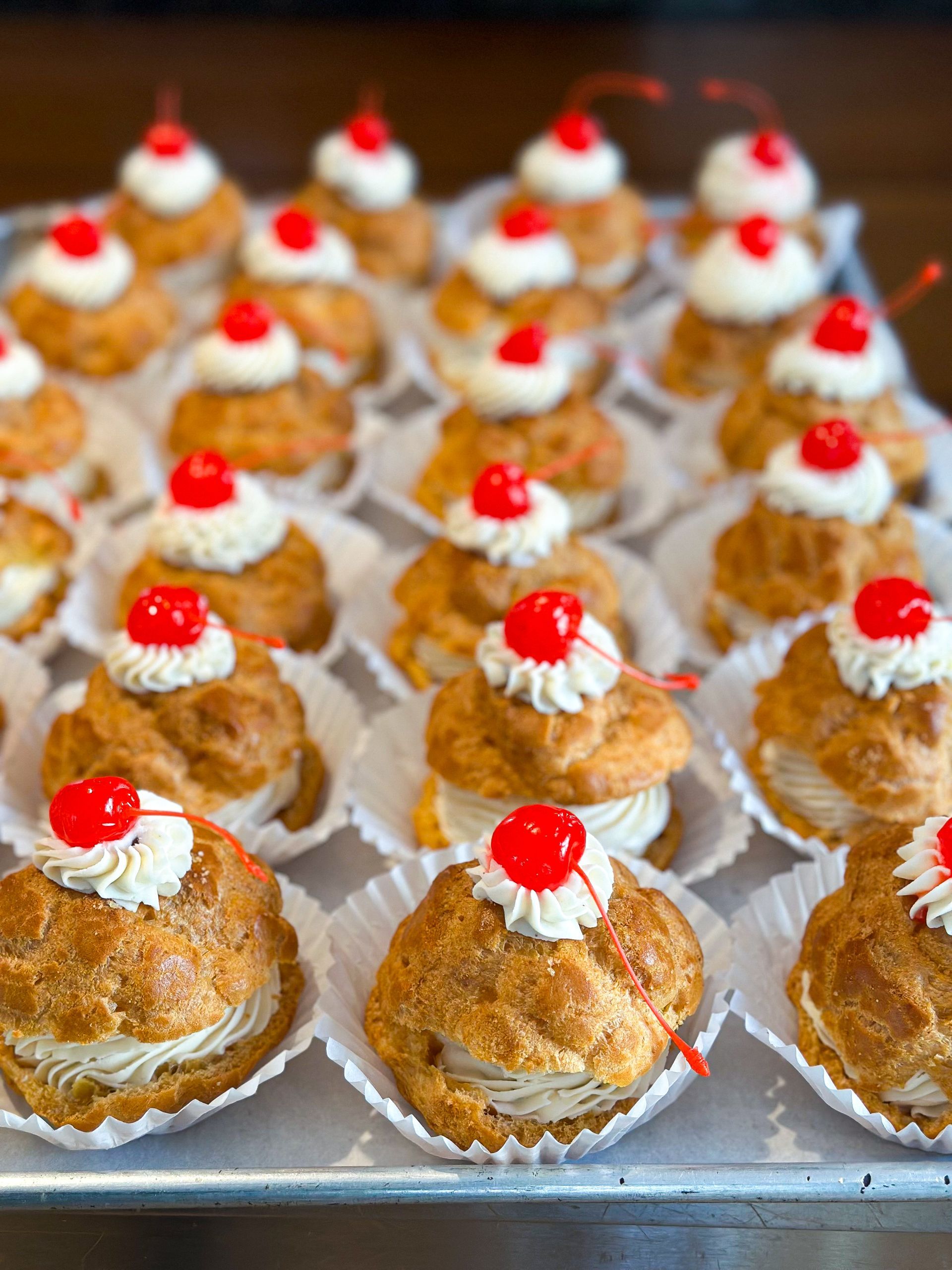 Tray of cream puffs topped with whipped cream and cherries.