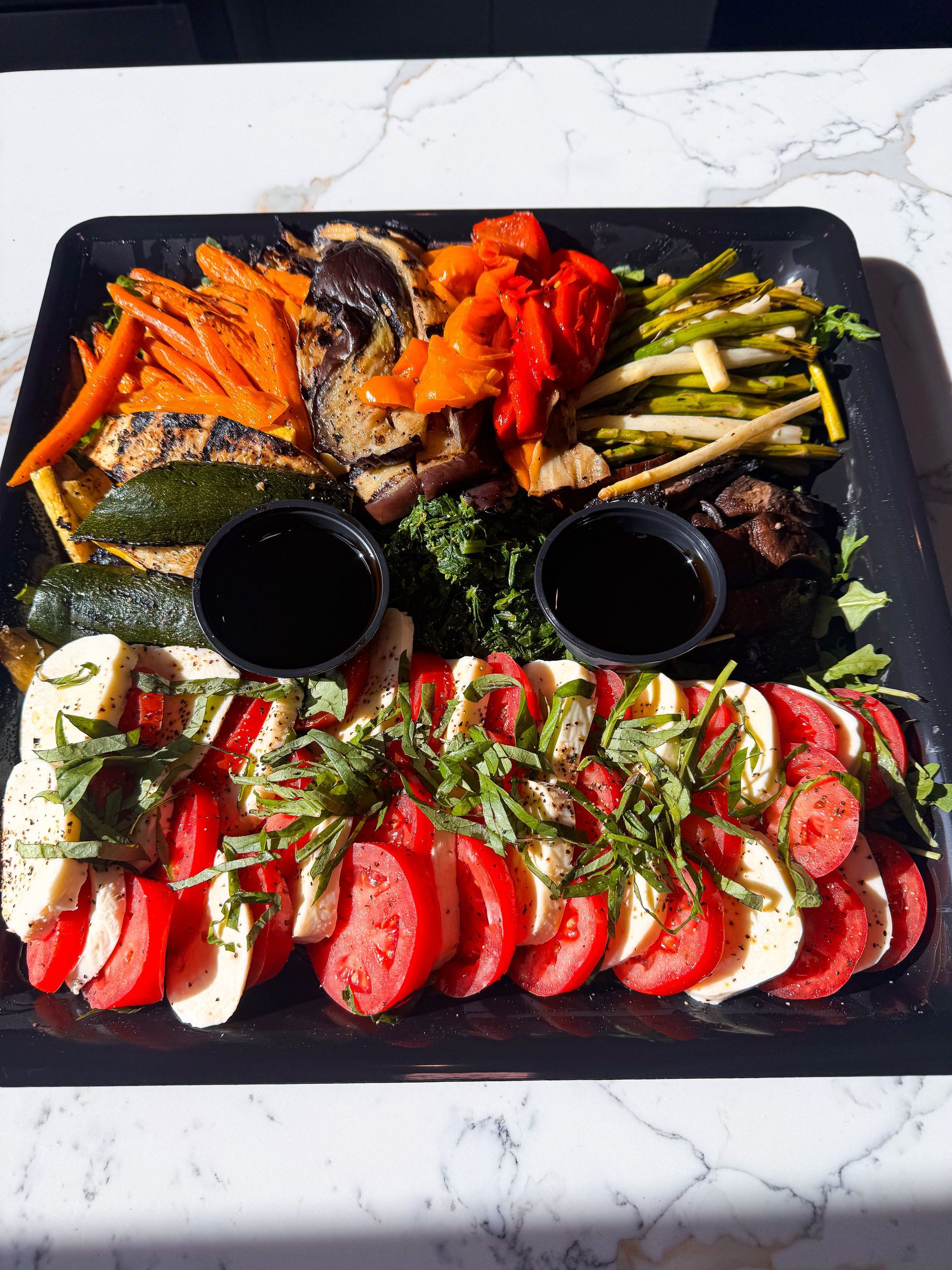 Platter with grilled vegetables, Caprese salad, and dipping sauces.