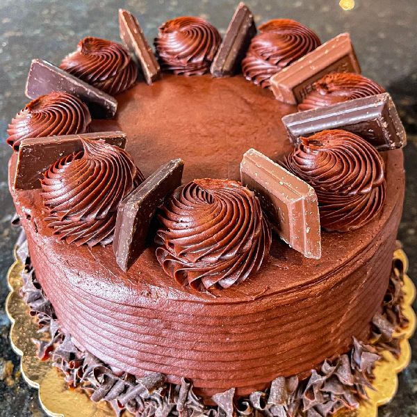 Chocolate cake with chocolate frosting, rosettes, and chocolate bar pieces.