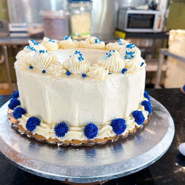 White frosted cake with blue frosting accents and sprinkles on a silver cake stand.