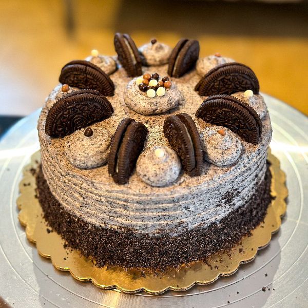 Oreo cookie cake with cream frosting and cookie crumbs, decorated with Oreo cookies and sprinkles, on a gold cake board.