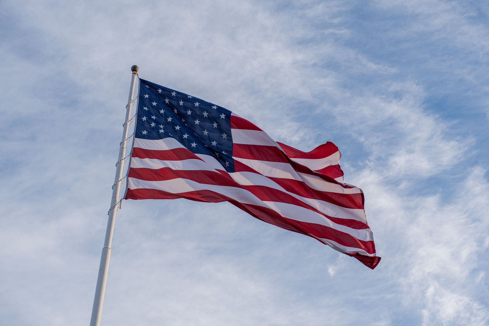 American flag waving on a flagpole against a cloudy sky